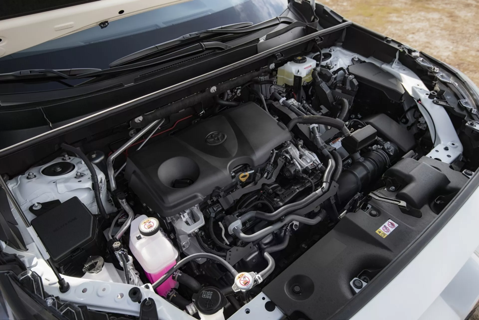 Detailný pohľad na motorový priestor Toyota RAV4 2019, ktorý zvýrazňuje čistý, moderný dizajn a komponenty, ako je kryt motora so znakom značky, systém prívodu vzduchu, batéria, nádrž na brzdovú kvapalinu a chladiaca nádrž, spolu s rôznymi potrubiami a káblovými zväzkami, pod otvorenou kapotou z uhla.