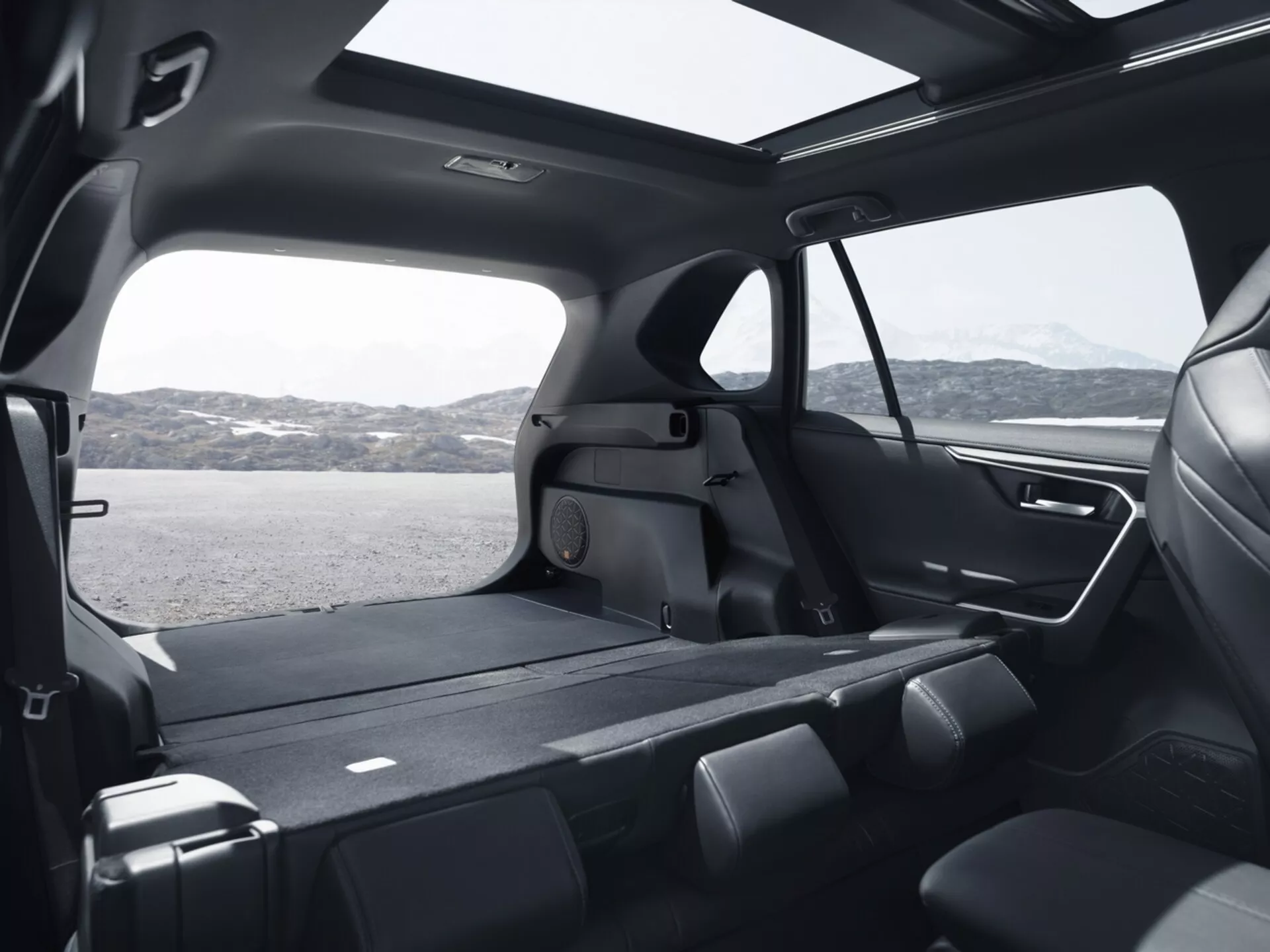 Interiérový pohľad na Toyota RAV4 2019 ukazujúci priestrannú zadnú kabínu z vysokého uhla, zdôrazňujúci sklopné sedadlá druhého radu, rozsiahly nákladný priestor, veľké tónované okná, moderný dizajn s prémiovými materiálmi, panoramatické strešné okno, pokročilé osvetlenie a funkcie klimatizácie