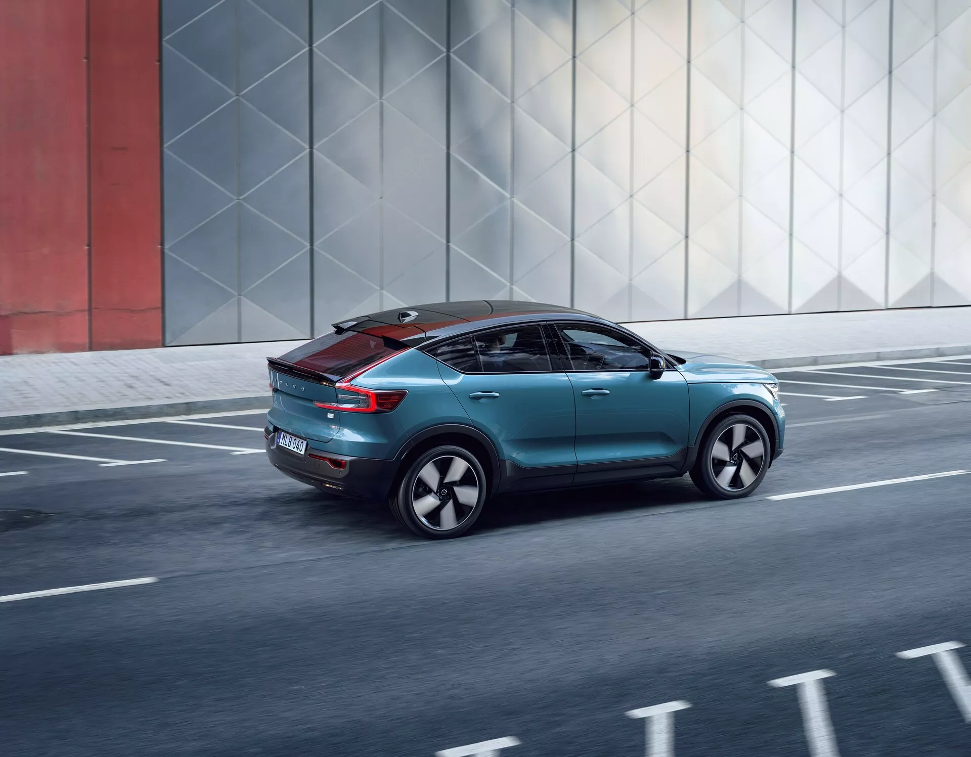 Dynamický pohľad zozadu troch štvrtín na Volvo C40 2021, ktorý ukazuje jeho elegantný dizajn, aerodynamické prvky, moderné zadné svetlá, špeciálne kolesá a panoramatickú strechu, počas jazdy na mestskej ceste.