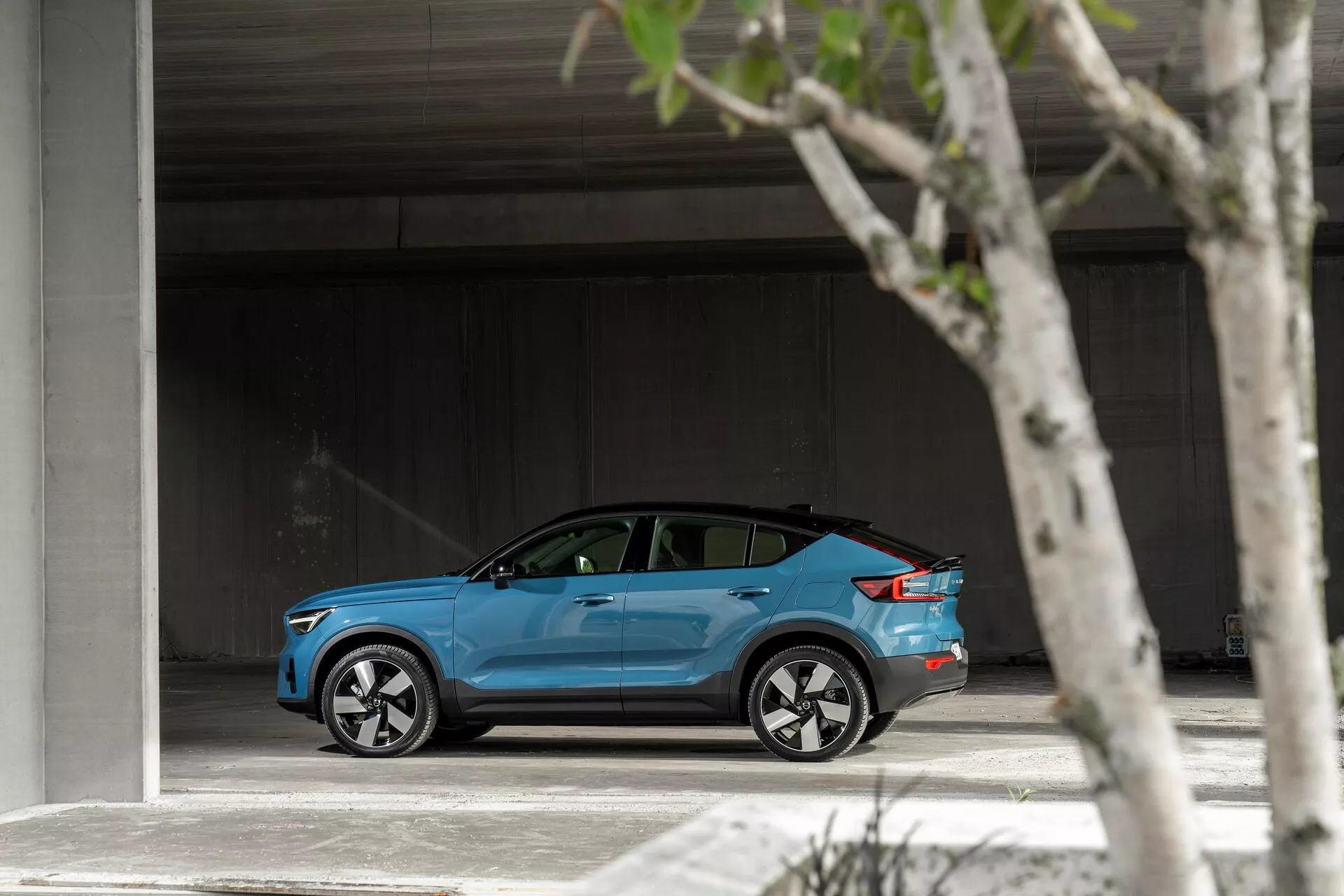 Bočný profil jasne modrého Volvo C40 z roku 2021 zaparkovaného v priestrannej oblasti, predvádzajúceho svoj elegantný, moderný dizajn, strieborné viaclúčové zliatinové kolesá, mierne zatmavené okná a potenciálny kryt nabíjacieho portu.