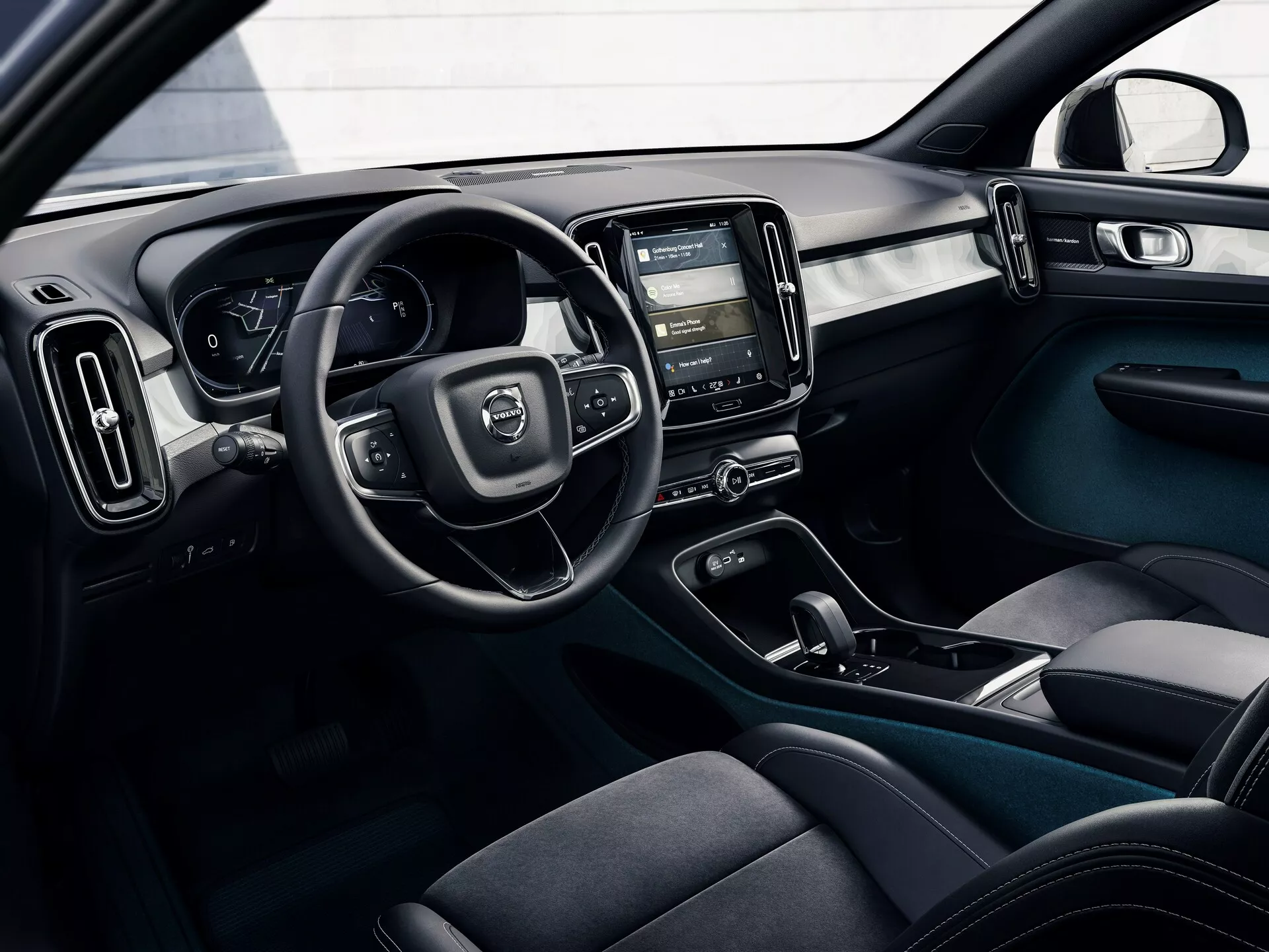 Fotografia interiéru vozidla Volvo C40 z roku 2021 (1. generácia) z vonkajšej perspektívy, zobrazujúca kokpit vodiča s volantom, digitálnym prístrojovým panelom, stredovou konzolou s dotykovým infotainment systémom, ovládaním klímy, ergonomickými sedadlami s tmavou látkou, tlačidlami ovládania dverí a dvojfarebným schémou s modernými a funkčnými dizajnovými prvkami.