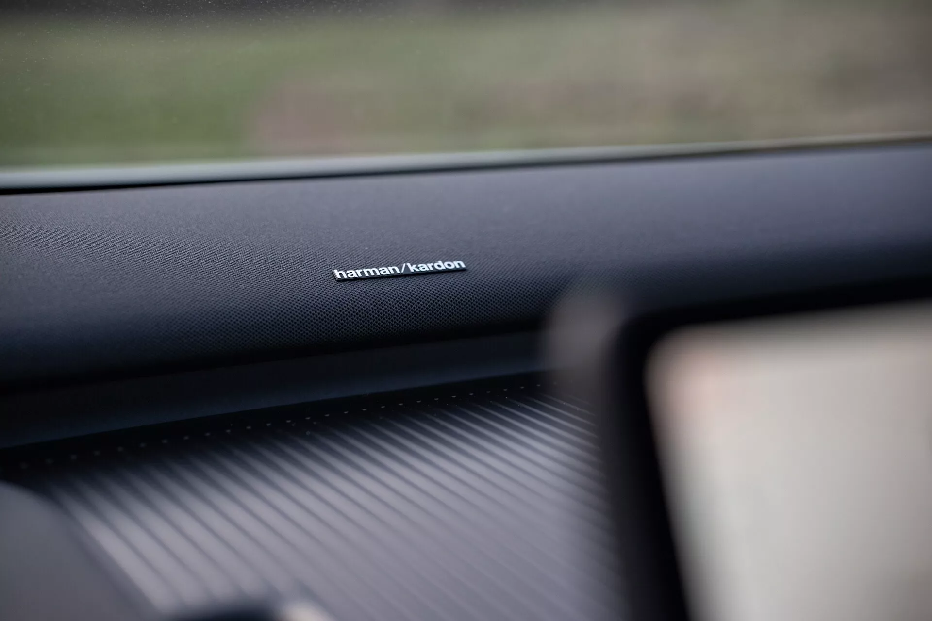 Interiérový záber Volvo EX30 2024 so zameraním na značenie audio systému Harman/Kardon na palubnej doske na strane spolujazdca, ktorý prezentuje materiál vysokej kvality a zdôrazňuje prednú technológiu zvukového systému.