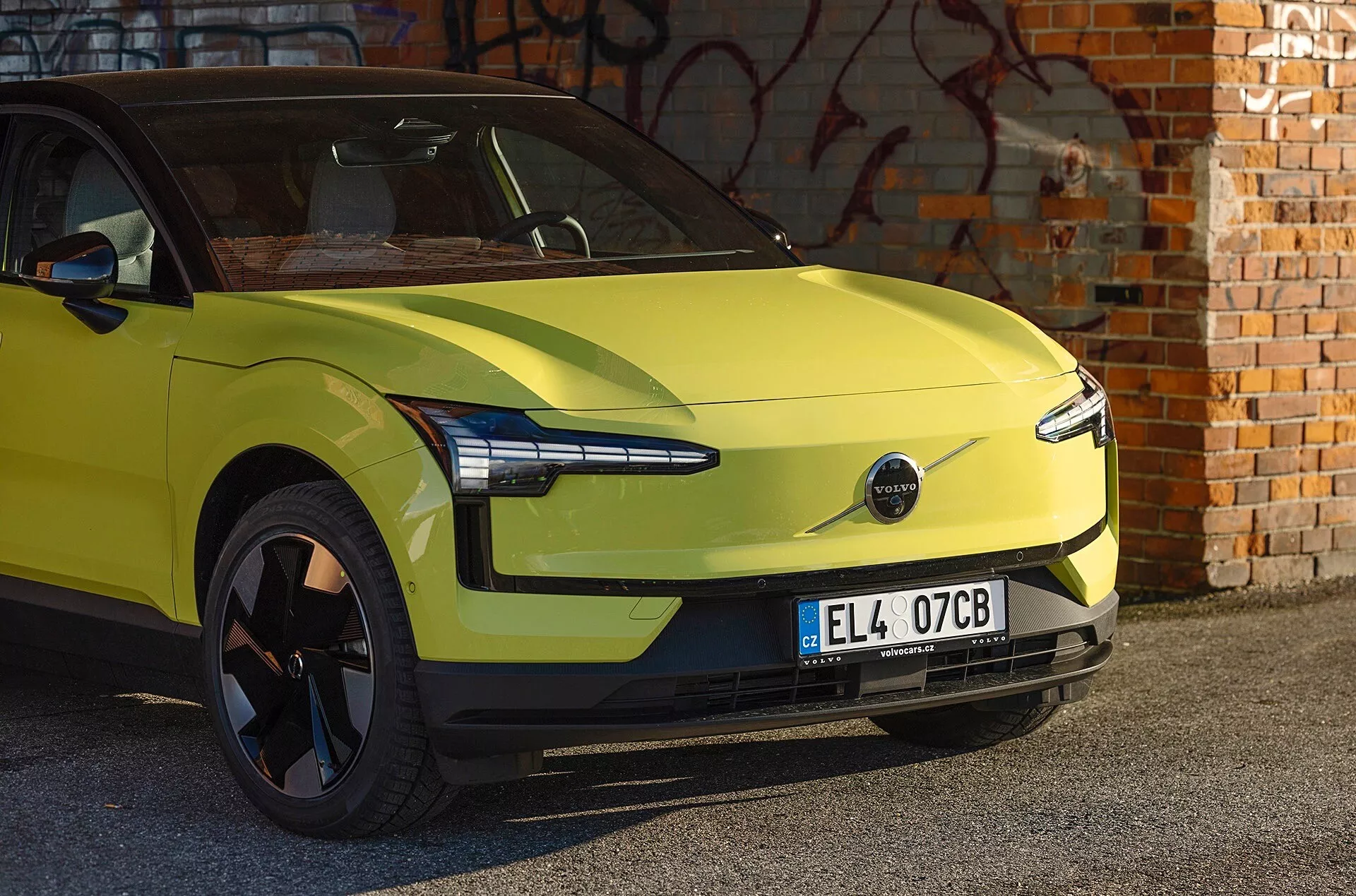 Elektrické auto Volvo EX30 v limetkovo zelenej farbe ročník 2024 zaparkované pred múrom s graffiti, predvádza aerodynamický dizajn, moderné LED svetlomety a absenciu prednej mriežky