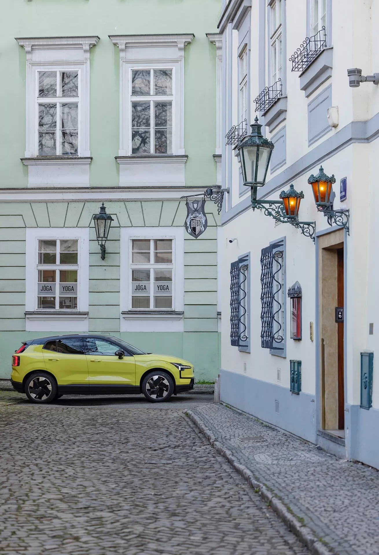 Volvo EX30 2024 zaparkované na dlažobnej ulici v prostredí starého mesta, zachytené z trojštvrťového zadného uhla zobrazujúceho pravú stranu a zadnú časť auta vrátane kolies, zadných svetiel a čiastočných detailov strechy vo svetlo žltej farbe