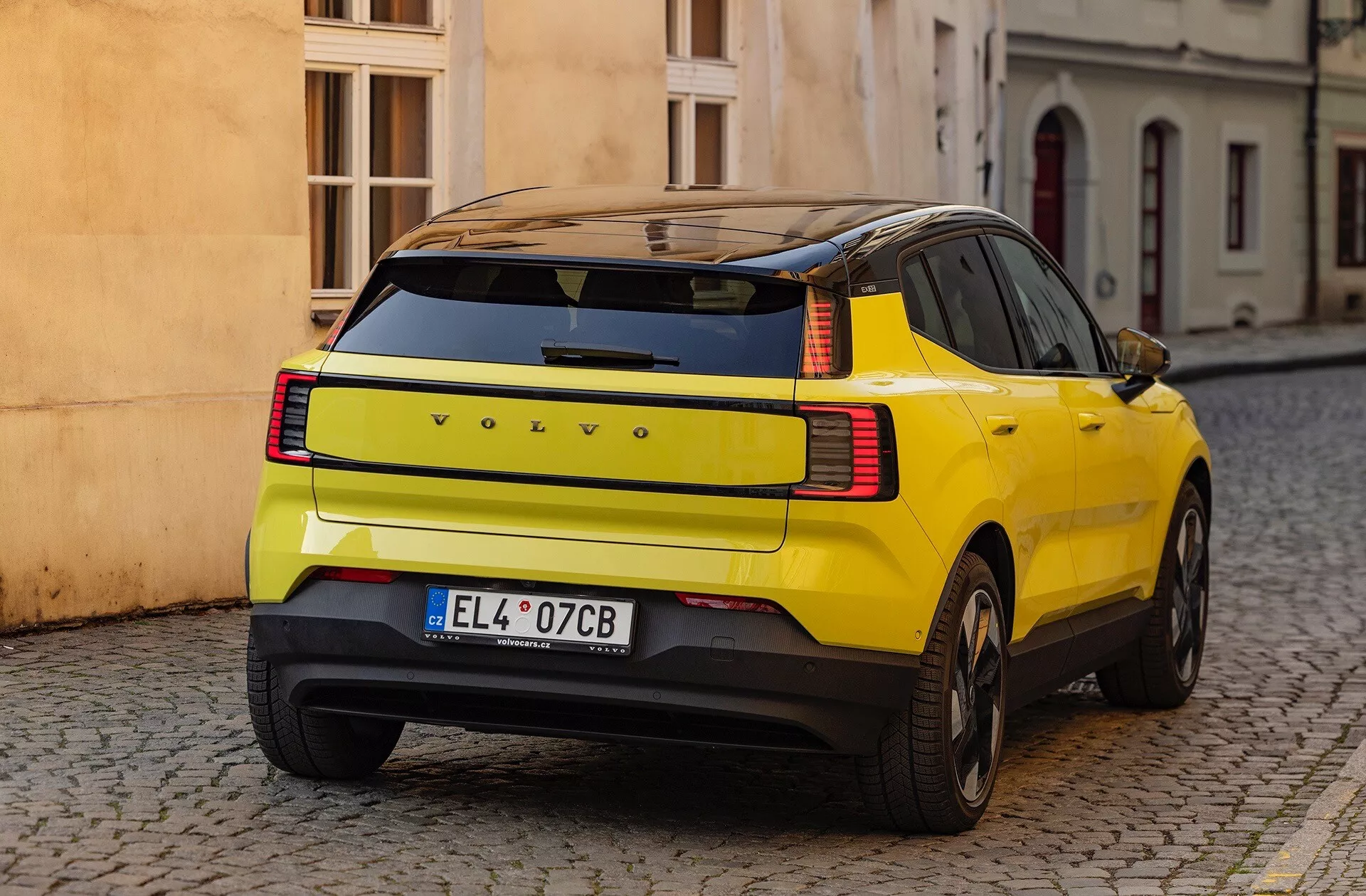 Žlté SUV Volvo EX30 2024 ukazuje svoje charakteristické zakrivenie zadného blatníka, LED zadné svetlá a bezpečnostné prvky, zaparkované na dlažobnej ulici z trojštvrťového zadného pohľadu