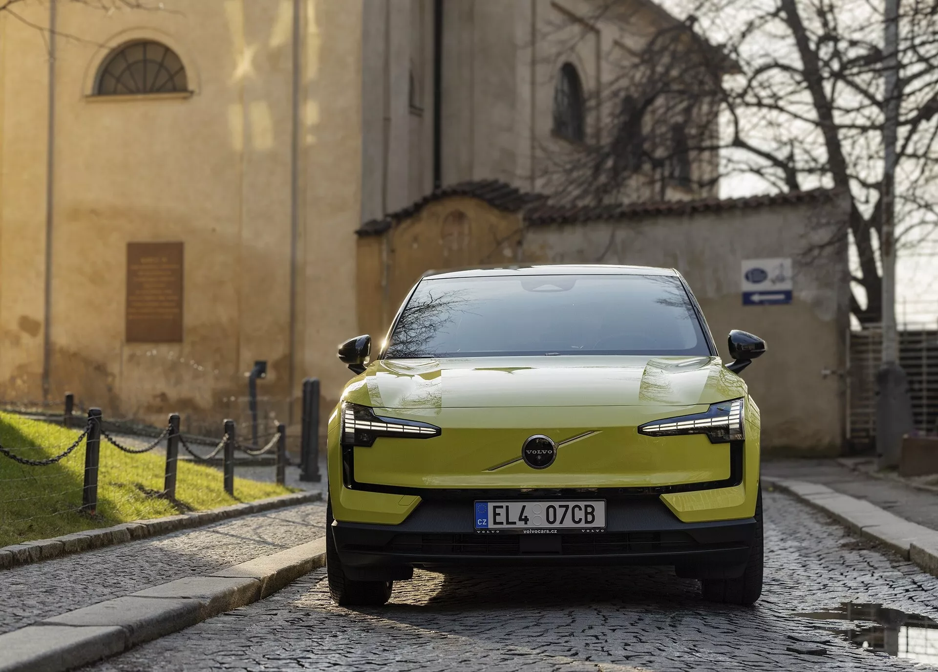 Moderné elektrické auto Volvo EX30 rok 2024 v chartreuse farbe, zaparkované na dlažobnej ulici, zobrazené z pravého predného uhla s LED svetlometmi a aerodynamickým dizajnom kapoty s históriou európskeho pozadia.