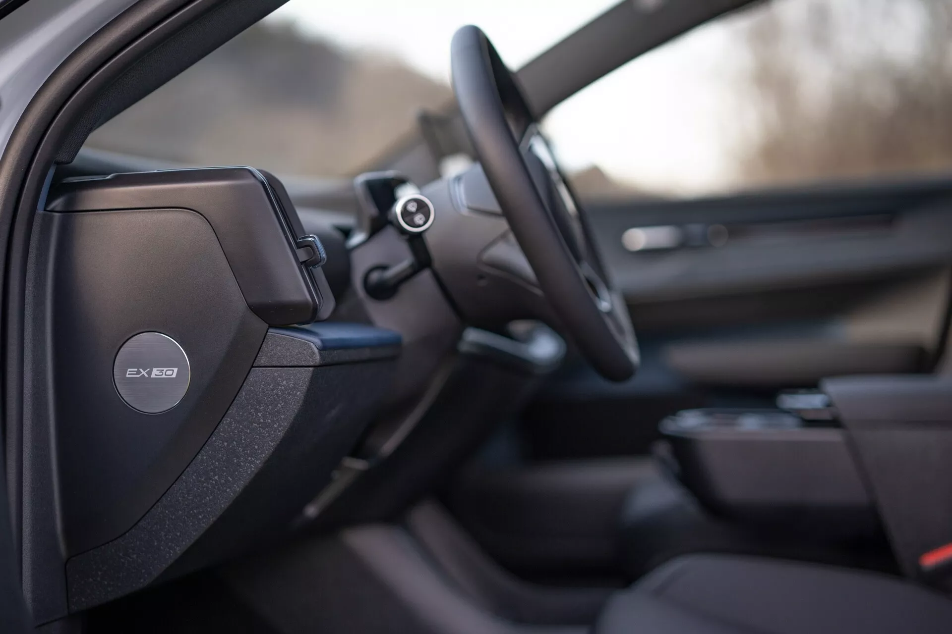 Interiérový pohľad na Volvo EX30 2024 zameraný na stranu vodiča s detailným športovým alebo prémiovým dizajnom sedadla, audio systém Harman Kardon na stĺpe B, multifunkčný volant a náznaky pokročilého informačného systému a dizajnu dverového panela spolujazdca