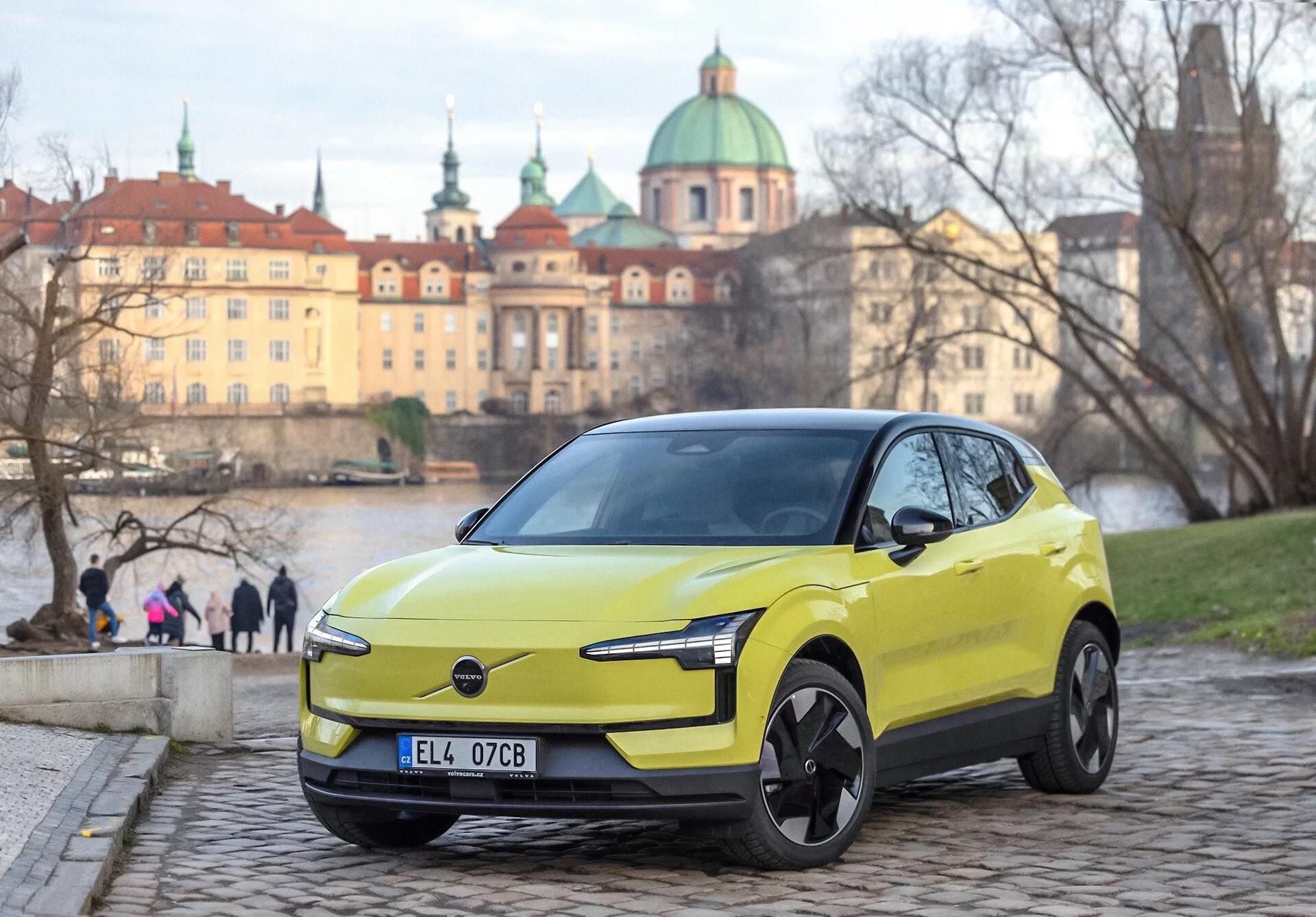 Lime zelené Volvo EX30 2024, pohľad z prednej časti pod uhlom tri štvrtiny na dlažobných kameňoch, s modernými LED svetlometmi a dizajnovými prvkami elektrického vozidla, mestské európske pozadie