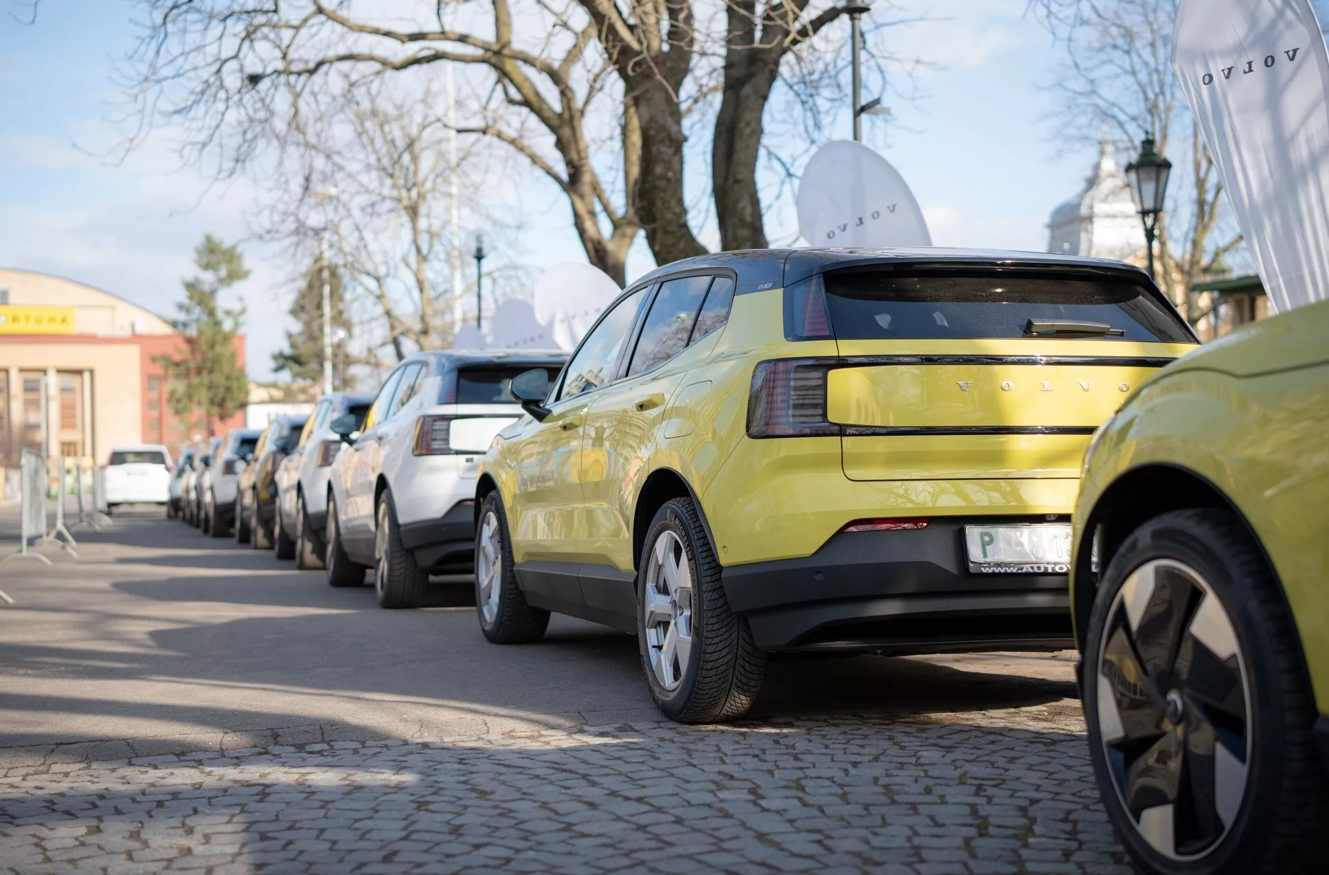 Limetkovo zelený Volvo EX30 z roku 2024 ukazujúci jeho zadnú časť s LED svetlami a zliatinovými kolesami s viacerými ramenami, zaparkovaný pozdĺž mestské ulice