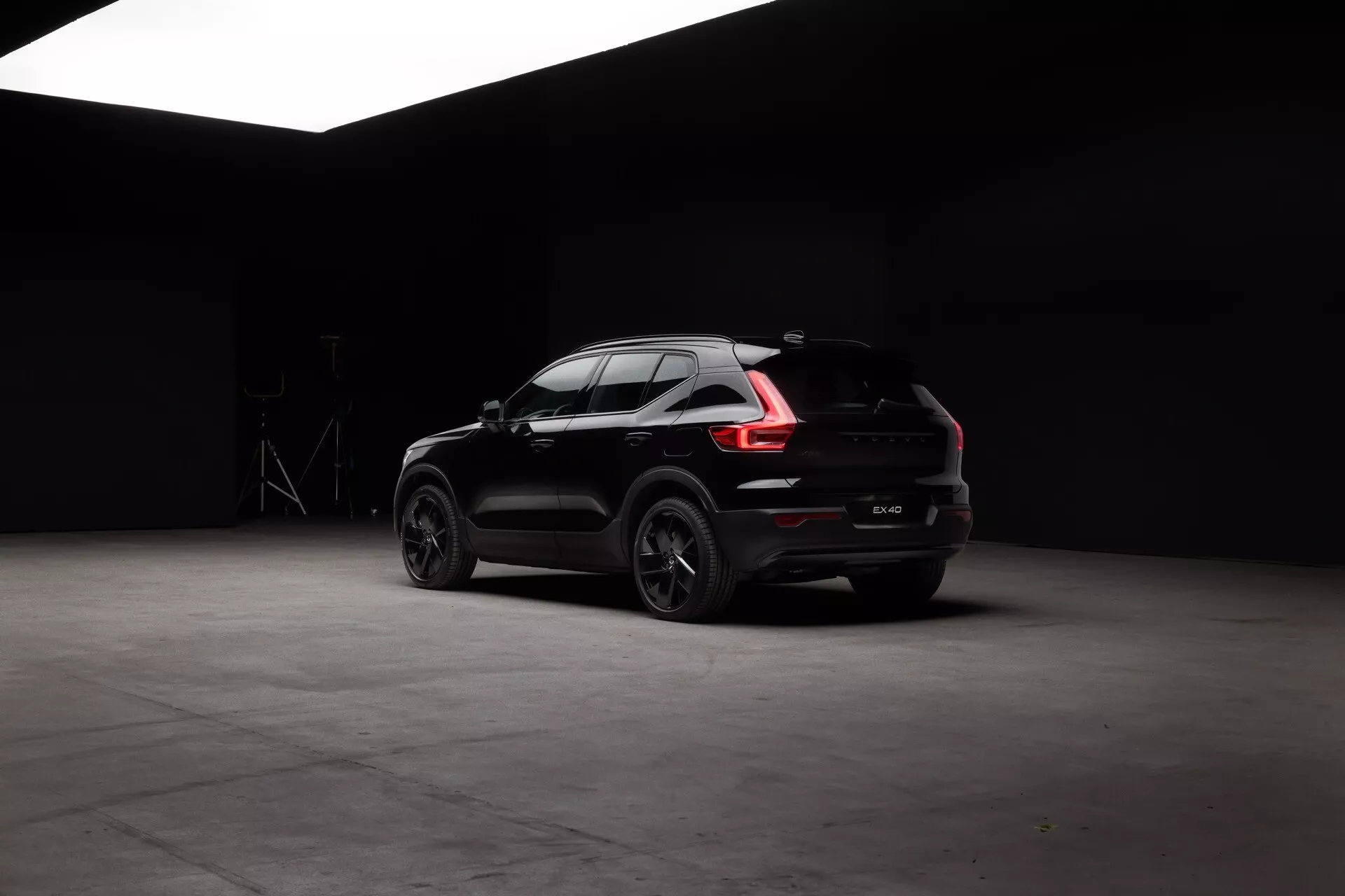 Čierny Volvo EX40 1. generácie rok 2024 s LED zadnými svetlami, športovým zadným dizajnom vrátane nárazníka a výfukov, veľkými zliatinovými kolesami s viacerými ramenami, matným povrchom laku a sklenenými oknami pre súkromie, zachytený z uhla odzadu tri štvrtiny v štúdiovom prostredí s tmavým pozadím, ktoré zvýrazňuje jeho štíhly, aerodynamický dizajn karosérie 'coupé SUV' a dizajnové prvky