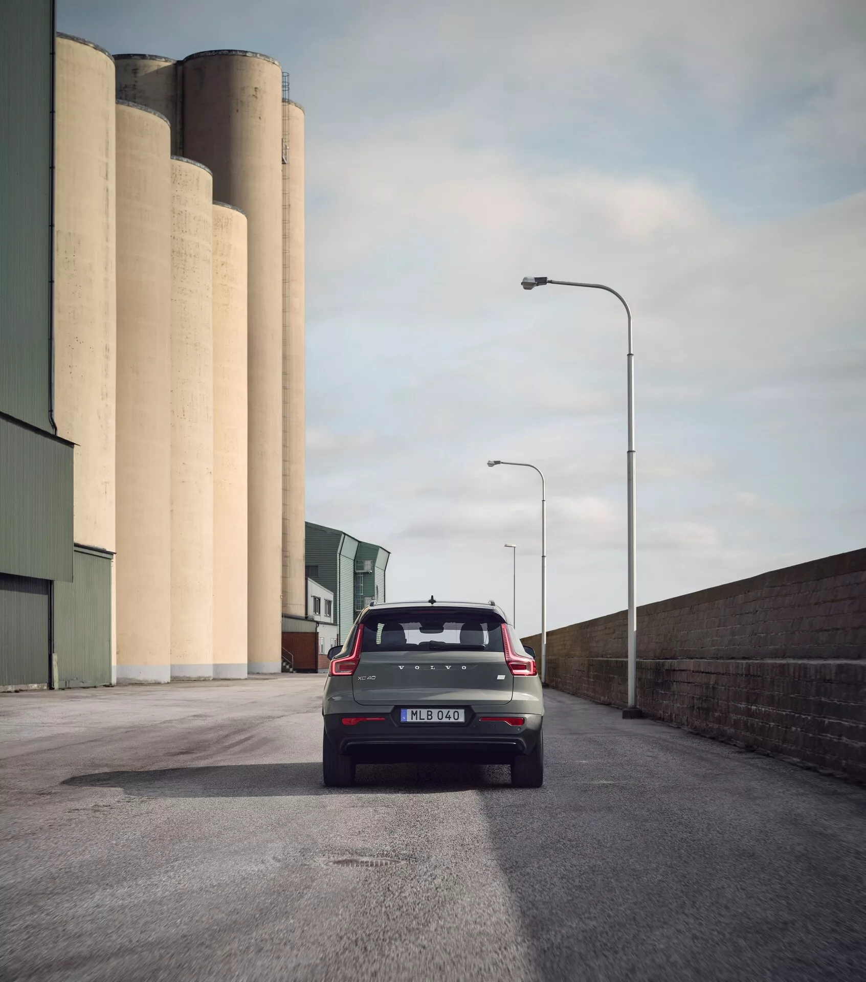 Zadný pohľad na Volvo EX40 1. generácie 2024 na asfaltovej ceste, moderný hatchback so zadným stieračom, anténou v tvare žraločej plutvy, spojlerom, súčasnými zadnými svetlami, parkovacími senzormi a dvojitým výfukom