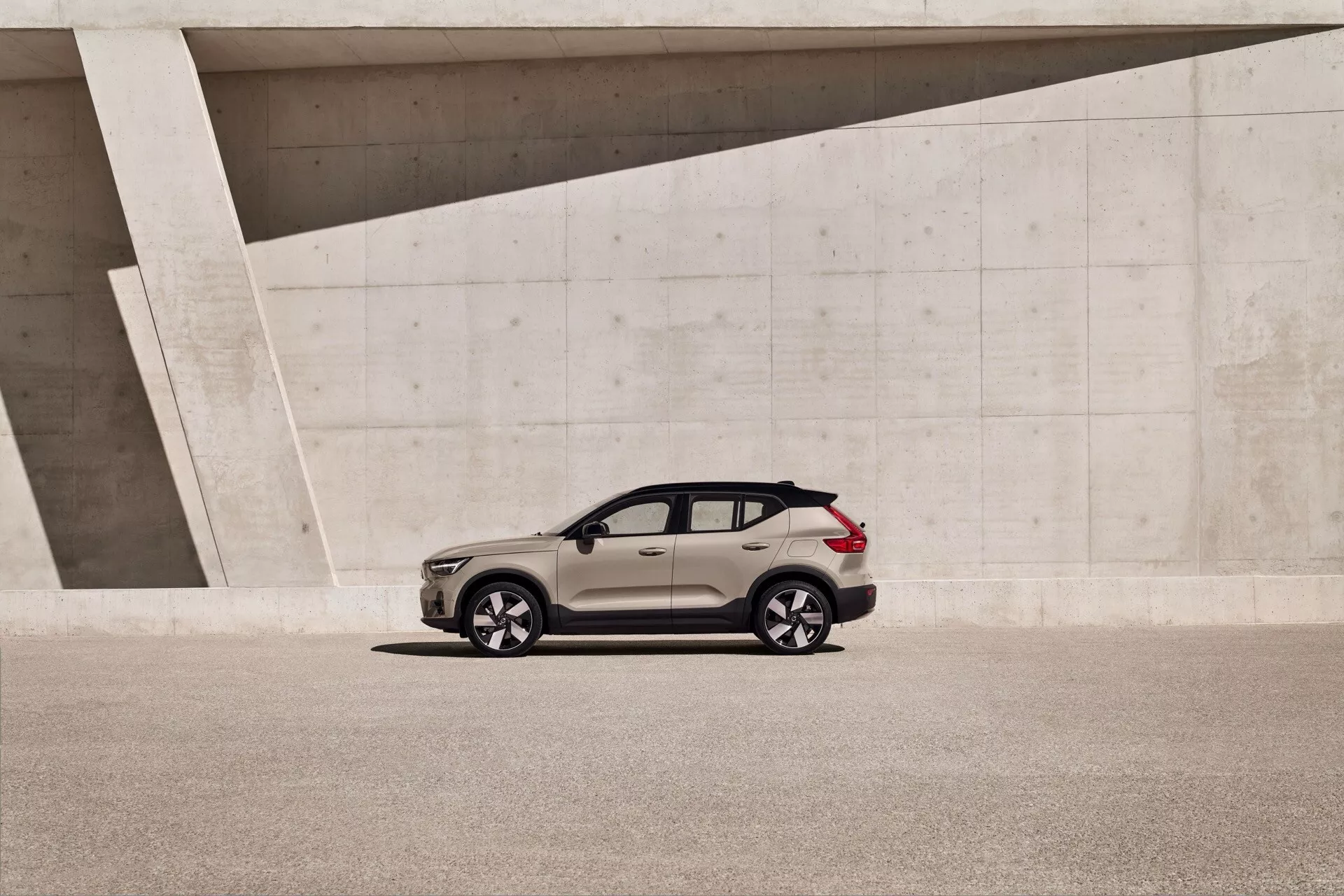 Volvo EX40 1. generácia 2024, moderné crossover SUV zaparkované vedľa uhlové betónovej štruktúry, zobrazujúce celý bočný pohľad s prirodzeným osvetlením a detailnými dizajnovými prvkami ako sú zliatinové kolesá a spádová línia strechy.