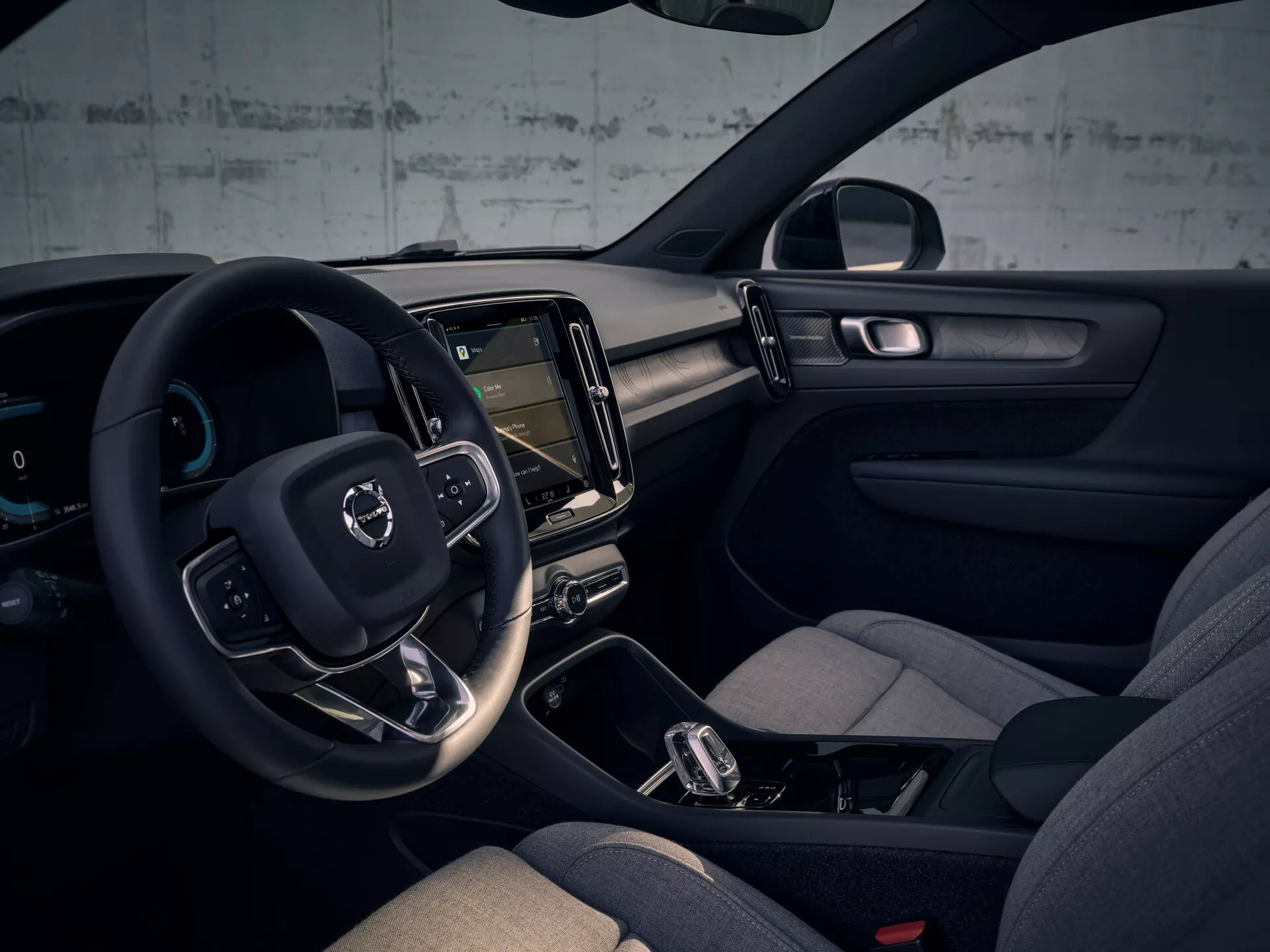 Interiér Volvo EX40 1. generácie pre rok 2024 s volantom na ľavej strane, digitálnym prístrojovým panelom, vertikálnym dotykovým infotainment systémom, minimalistickým dizajnom palubnej dosky, pohodlnými sedadlami so stranovým vyztužením, automatickou prevodovkou s možnosťou manuálneho radenia, integrovaným ambientným osvetlením, farebnou schémou v tmavých tónoch a pokročilými technologickými prvkami.