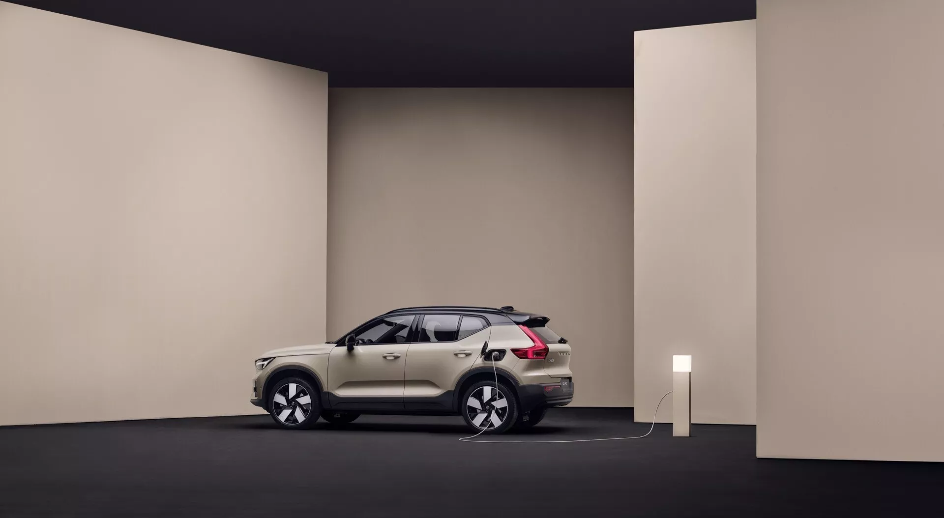 Volvo EX40 1. generácie 2024 v štúdiovom prostredí ukazuje jeho elegantný dizajn, bielu alebo striebornú farbu, pripojenie k nabíjacej stanici naznačuje funkcie elektrického vozidla, umiestnené tak, aby bolo vidieť profil a prednú časť auta