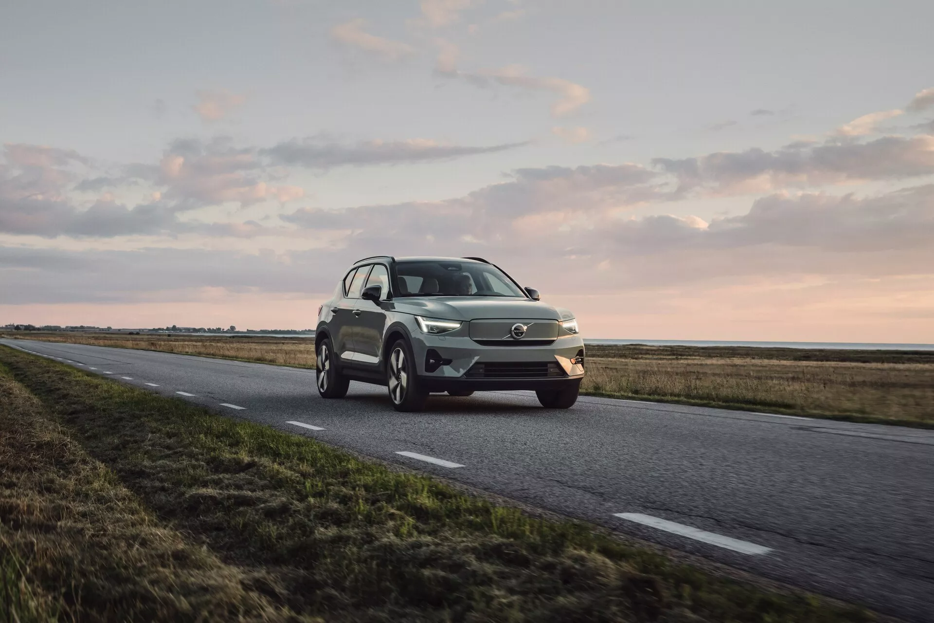 Volvo EX40 2024 1. generácia v dynamickom pohľade spredu a z boku, predvádzajúce LED svetlomety, charakteristickú mriežku, zliatinové kolesá a moderný dizajn SUV v metalickej farbe pri jemnom prírodnom svetle