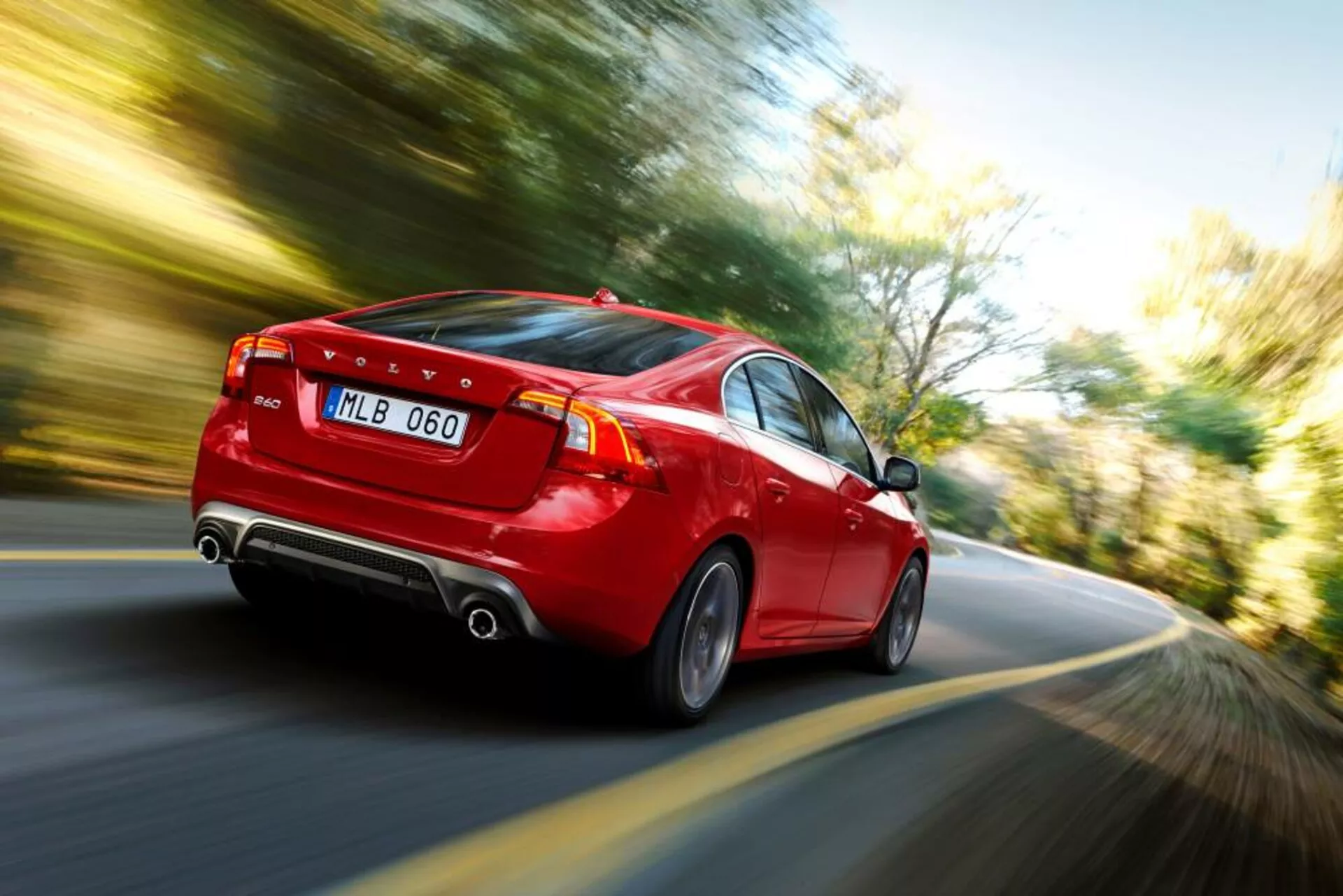 Dynamický zadný trojštvrťový pohľad na červený sedan Volvo S60-V60 2004 v pohybe, zobrazuje LED zadné svetlá, dvojitý výfuk, štýlové zliatinové kolesá a jasný indikátor rýchlosti prostredníctvom efektu rozmazania pohybu.