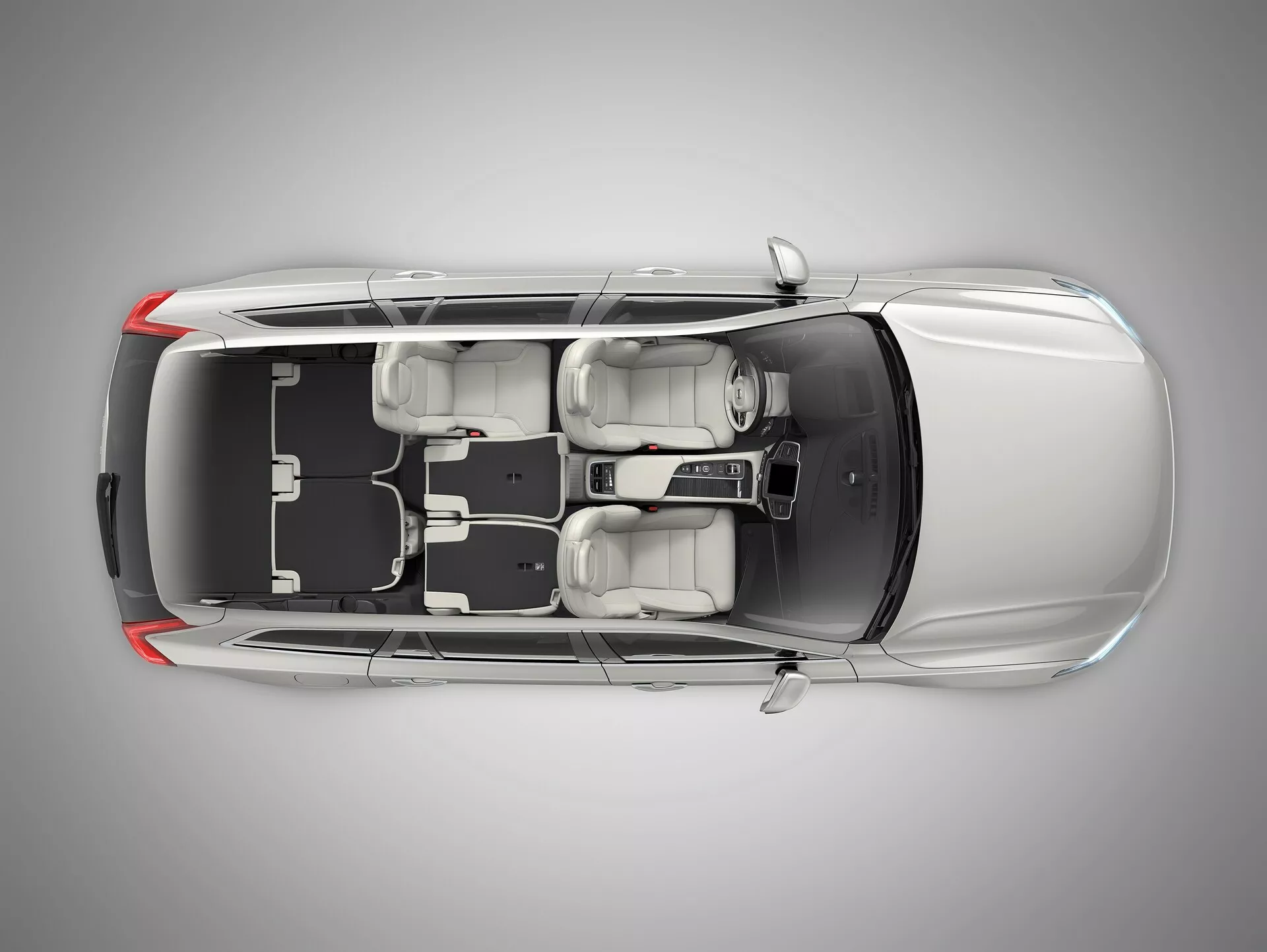 Pohľad z vtáčej perspektívy na sedan Volvo XC90 druhej generácie z roku 2015 s priesvitnou alebo digitálne odstránenou strechou, ktorý odhaľuje interiér. Obrázok ukazuje dlhú kapotu, štyri zatvorené dvere, štyri kolesá a usporiadanie sedadiel s dvoma prednými sedadlami a zadnou lavicou pre troch cestujúcich. Viditeľná stredová konzola a radiaca páka. Zobrazené usporiadanie ľavého riadenia s volantom, displejom a ovládacími prvkami na palubnej doske. Sú zreteľné dizajnové prvky ako opierky hlavy, vonkajšie zrkadlá a celkový vnútorný priestor a usporiadanie.