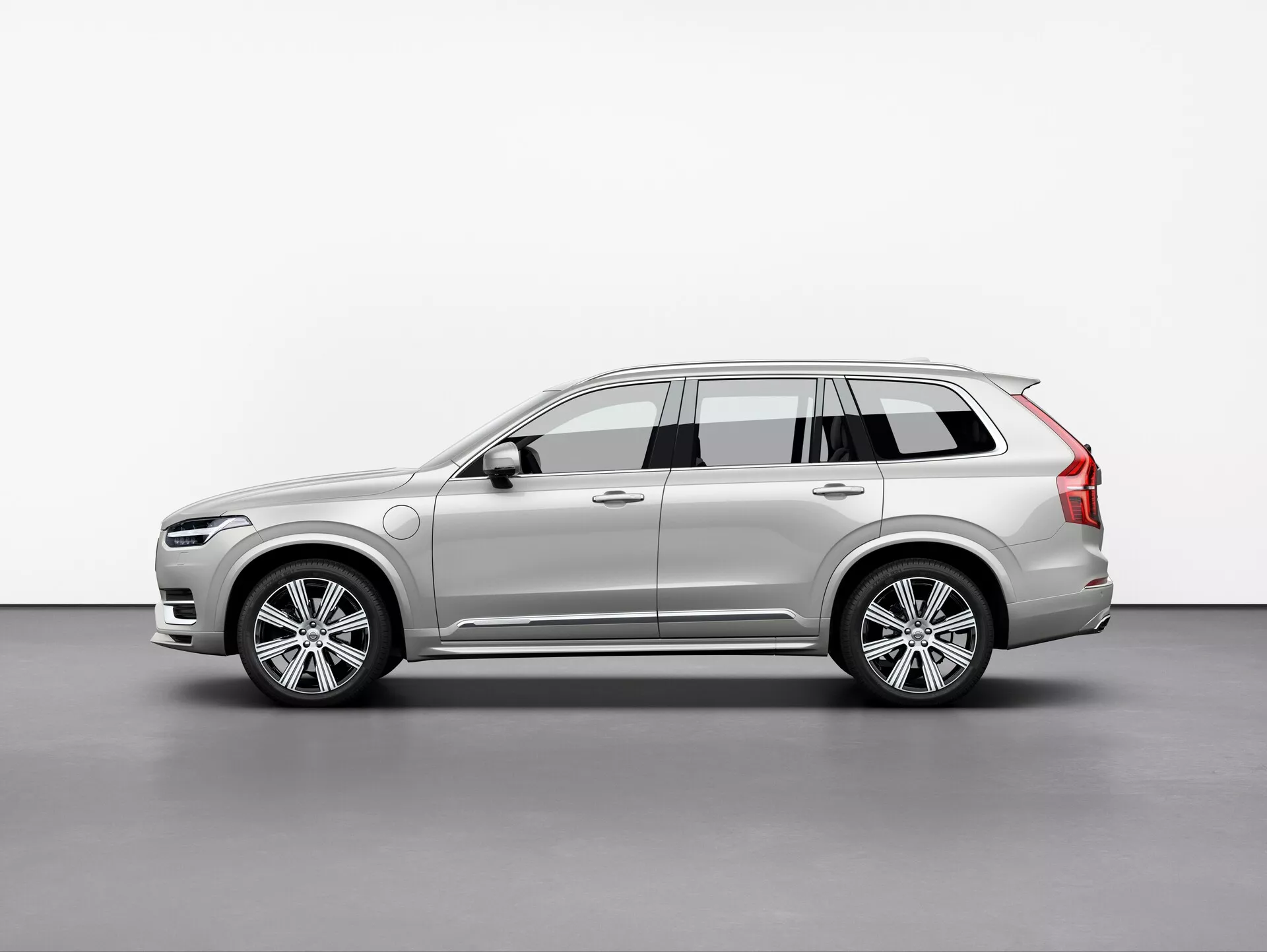Obrázok SUV Volvo XC90 2015, fotografovaný z trojštvrťového pohľadu pod miernym uhlom. Tento pohľad zvýrazňuje predné aj bočné profily, ktoré ukazujú elegantný a moderný dizajn auta, zložité LED svetlomety, čiastočne viditeľnú prednú mriežku, kolesá z hliníkovej zliatiny s viac paprskami, bočné zrkadlá s integrovanými smerovkami, strešné lyžiny, dynamické línie karosérie, lak a farbu. Mäkké osvetlenie v ateliérovom nastavení presne odráža kontúry a povrchové detaily vozidla.