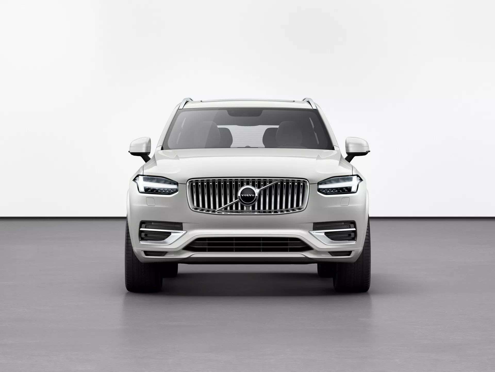 Predný pohľad na SUV Volvo XC90 2015 (2. generácia) proti bielemu pozadiu v štúdiovom prostredí, ktoré zvýrazňuje zvýšenú svetlosť, veľkú mriežku s vertikálnymi pruhmi so znakom Volvo, elegantné LED svetlomety 'Thorovo kladivo', definované línie kapoty, hmlovky na dolnom nárazníku a bočné zrkadlá s integrovanými smerovkami.