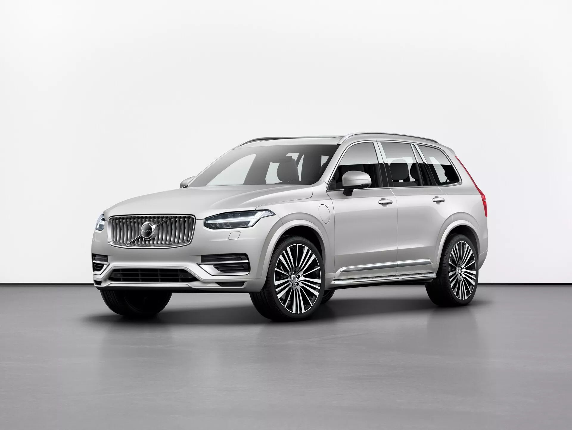 Ateliérová fotografia luxusného SUV Volvo XC90 2015 (2. generácia) zobrazená z trojštvrťového predného uhla, ukazujúca prednú mriežku s výrazným logom, elegantné LED svetlomety, značný predný nárazník a dlhý rázvor s veľkými zliatinovými kolesami. Bočné zrkadlá sú umiestnené pod stĺpikom A, s oknami orámovanými chrómovými lištami a strešnými nosičmi dodávajúcimi prémiový pocit. Neutrálna farba laku vyžaruje sofistikovanosť a obrázok zvýrazňuje línie a kontúry vozidla rovnomerným osvetlením na jednoduchom pozadí. Pravdepodobné vlastnosti zahŕňajú technológie asistencie pre vodiča a pokročilé infotainmentové systémy.