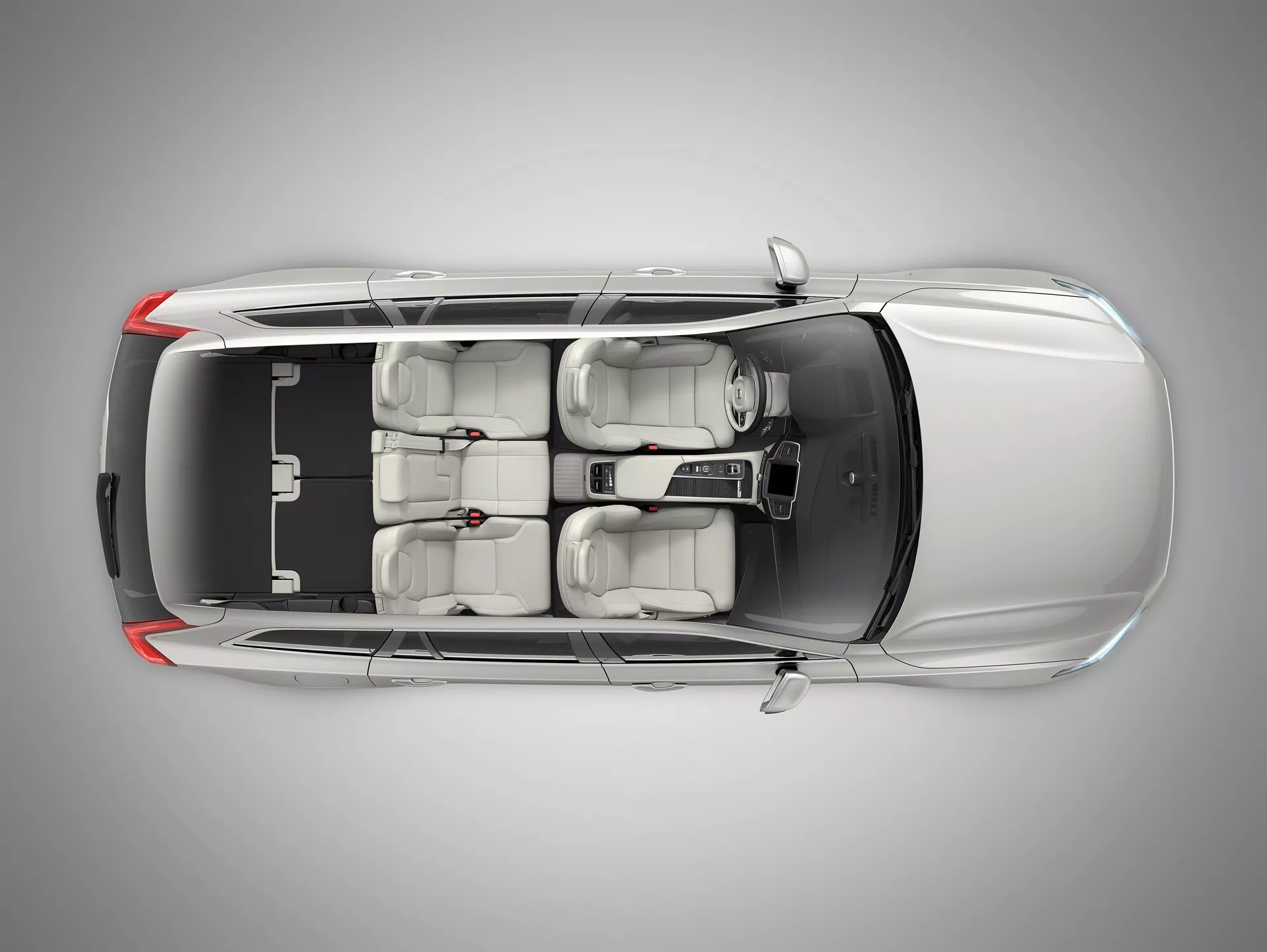 Pohľad zhora na kovový Volvo XC90 2015 ukazujúci kontrastnú čiernu strechu, aerodynamický dizajn, strešné okno, dve rady sedadiel s pokročilými nastaviteľnými prednými sedadlami, centrálnu ovládaciu konzolu a tónované okná, uprostred profesionálneho štúdia.