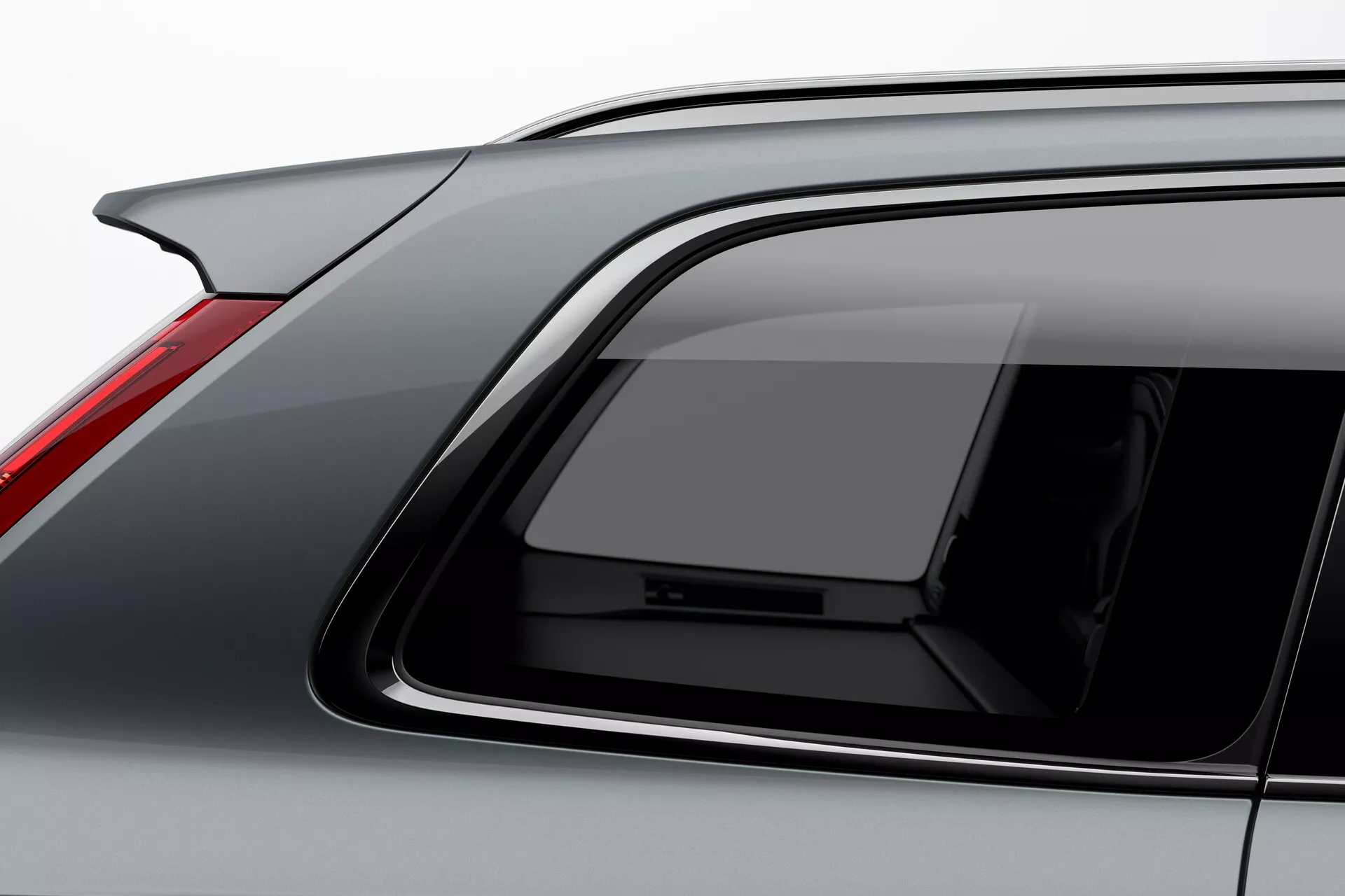 Detailný pohľad na Volvo XC90 2015 druhej generácie, zameraný na bočnú a zadnú časť z vyššieho uhla. Medzi vlastnosti patrí jemne klesajúca línia strechy, vysoko umiestnené stredové brzdové svetlo, luxusný dizajn zadného bočného okna, hrubý C-stĺpik s predným náklonom a vysokokvalitné úpravy detailov. Vozidlo je v neutrálnom šedom alebo striebornom odtieni s hladkým a lesklým lakom, zachytené mäkkým a rovnomerným osvetlením, ktoré ukazuje podrobné textúry a materiály. Ideálne na ilustrovanie automobilového dizajnu a luxusných funkcií.