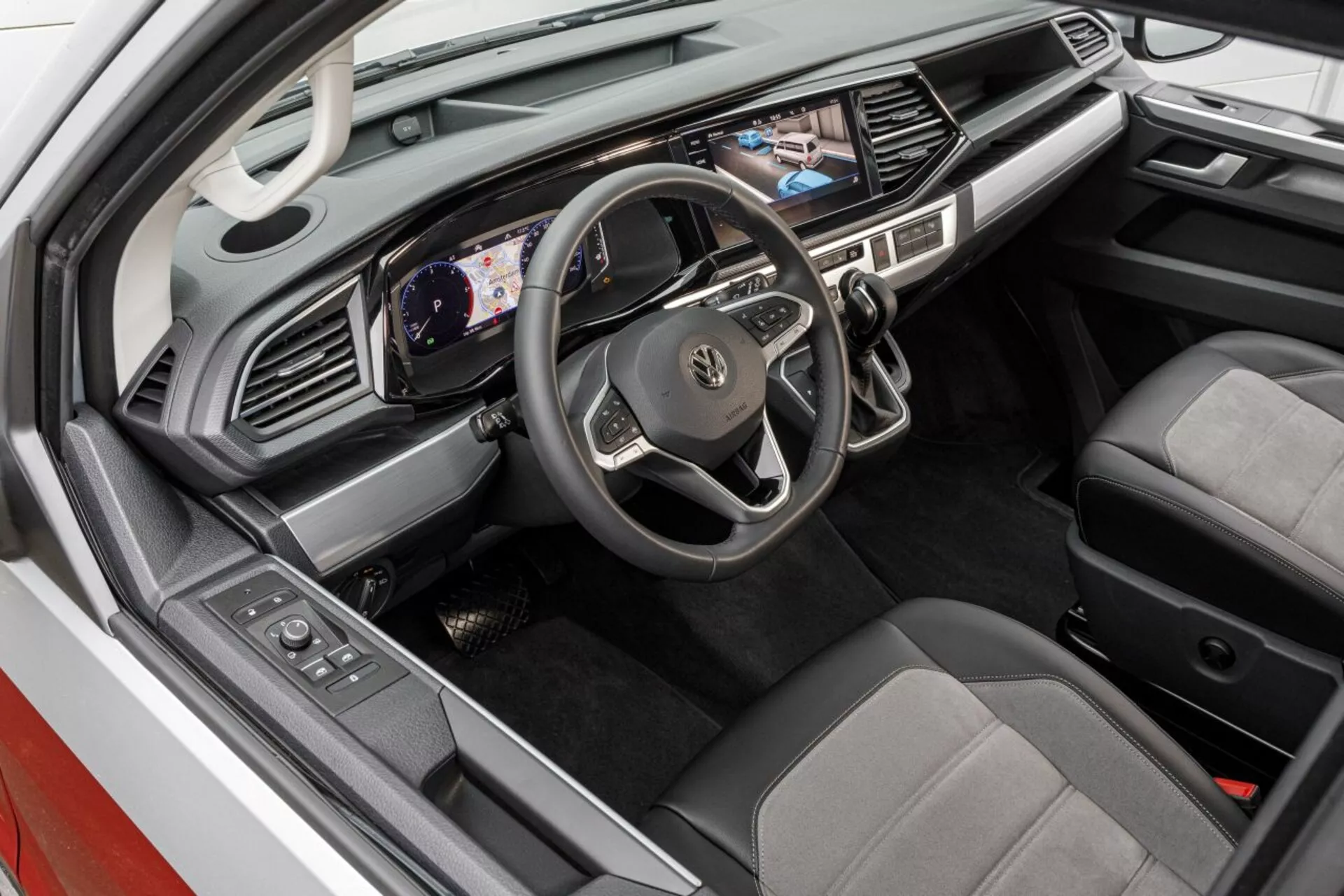 Zvýšený pohľad na interiér Volkswagen Nutzfahrzeuge Transporter 2019 (T6.1 California) ukazujúci priestor vodiča s digitálnym prístrojovým panelom, dotykovou obrazovkou multimédií a sedadlami v dvoch tónoch
