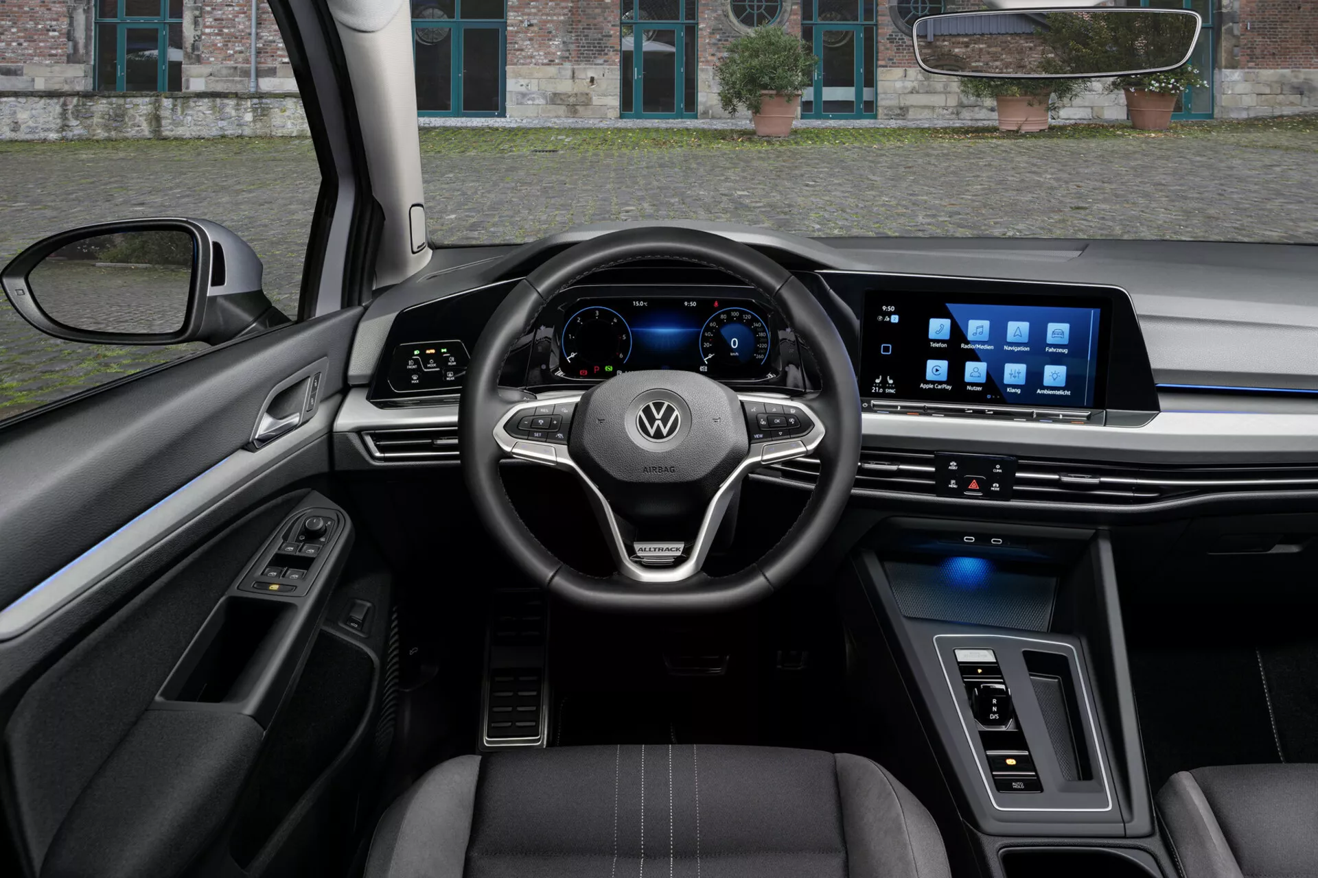 Interiér VW Golf Alltrack 2017 z pohľadu vodiča, ukazuje volant s tromi ramenami s ovládacími prvkami a logom Volkswagen, digitálny prístrojový panel a široký dotykový infotainment systém na palubnej doske, zdôraznený pokročilými technologickými funkciami, sedadlá potiahnuté kožou s kontrastným prešívaním a kombinácia luxusných materiálov a ambientného osvetlenia.