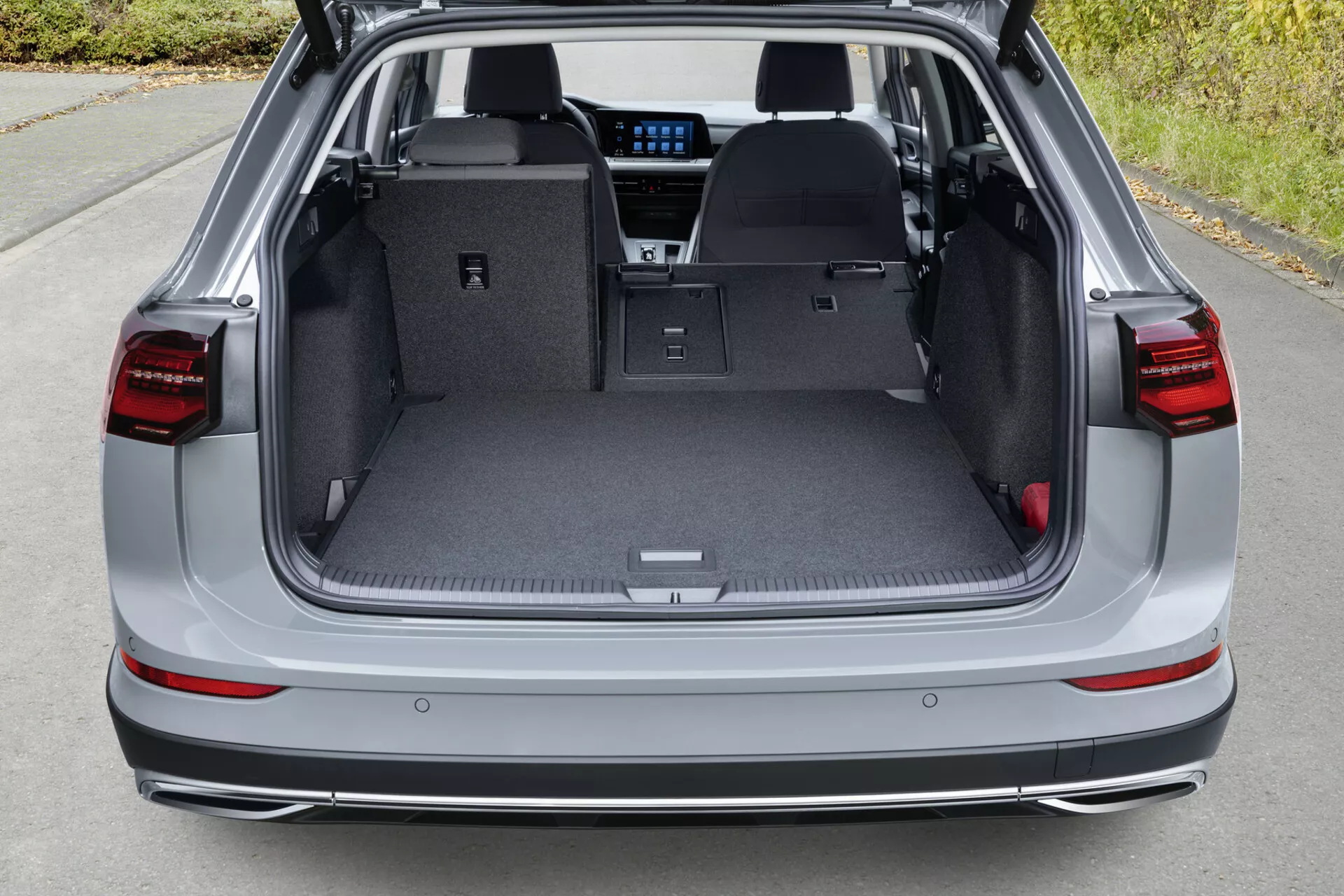Pohľad zhora na zadný nákladový priestor VW Golf Alltrack z roku 2017 s otvoreným vekom, zobrazujúci rovnú nákladnú podlahu so sklopenými zadnými sedadlami, LED zadné svetlá, parkovacie senzory na zadnom nárazníku a naznačenie modernej technológie infotainmentu cez zadnú časť.