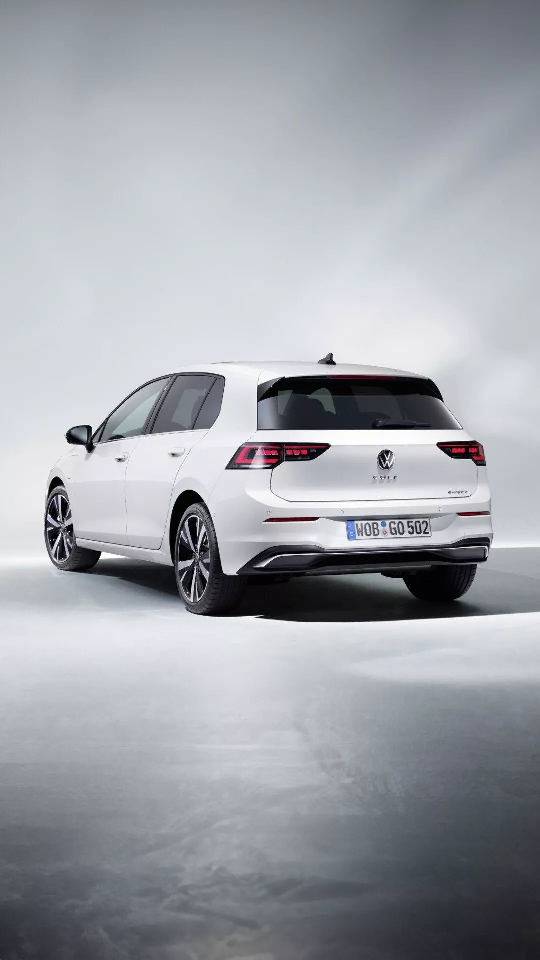Biele hatchback Volkswagen Golf (VIII Facelift) 2024, videnie z trojštvrtovej zadnej perspektívy ukazujúce LED zadné svetlá, dvojité výfuky, viaceročné zliatinové kolesá a zadný strešný spojler na pozadí štýlového štúdia