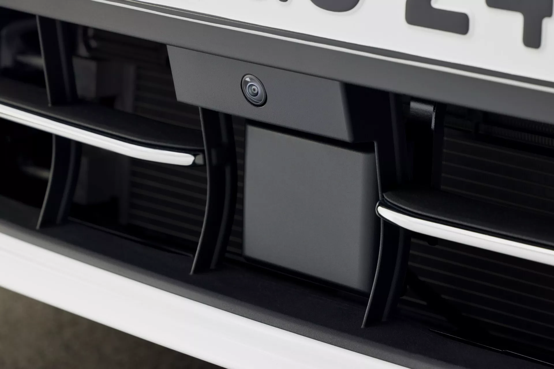 Detailný pohľad na časť mriežky a nárazníka VW Golf VIII po facelifte v roku 2024 s lesklými čiernymi horizontálnymi lamelami, chrómovými akcentami, športovo aerodynamickými prvkami, parkovacím senzorom alebo kamerou a uhlovými dizajnovými prvkami