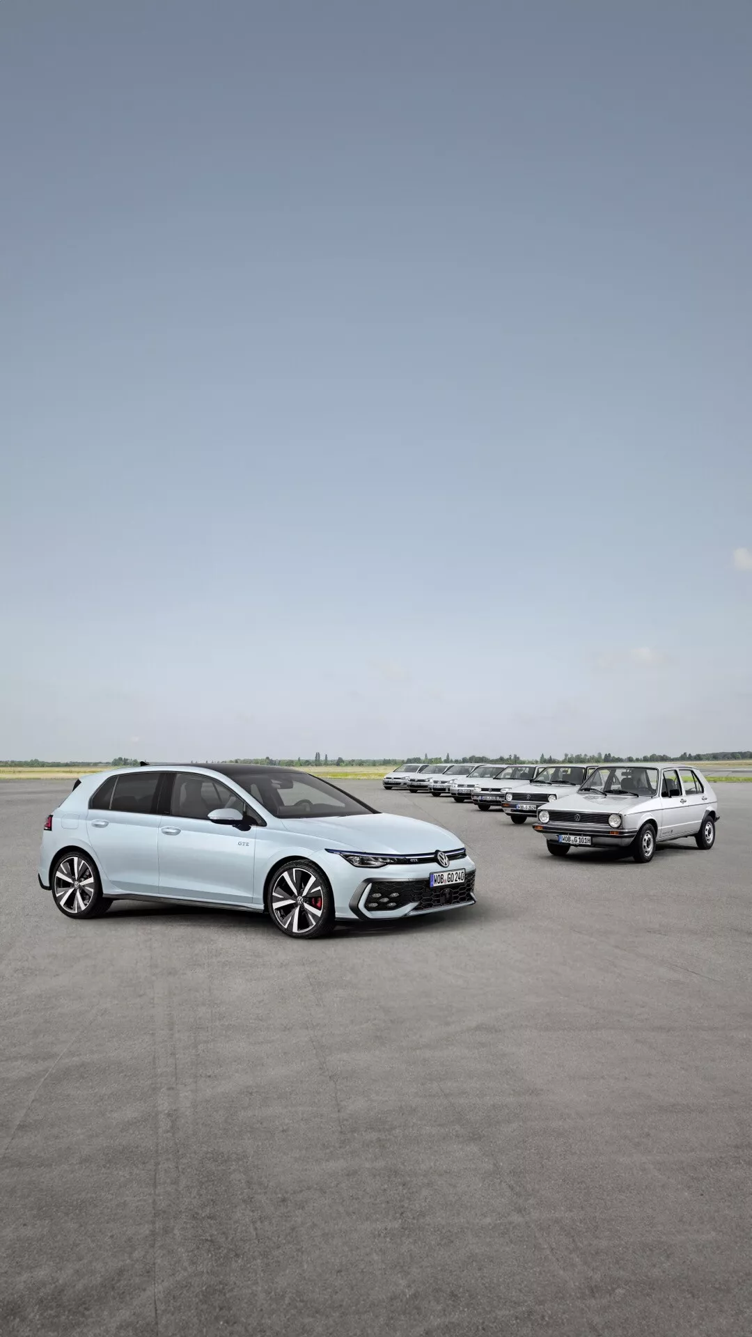 Pohľad z prednej a bočnej strany na facelift VW Golf VIII 2024 na otvorenom parkovisku, zdôrazňujúci dizajnové prvky ako LED svetlomety, zliatinové kolesá a pokročilé bezpečnostné funkcie, s radom áut na pozadí pod jasnou oblohou.