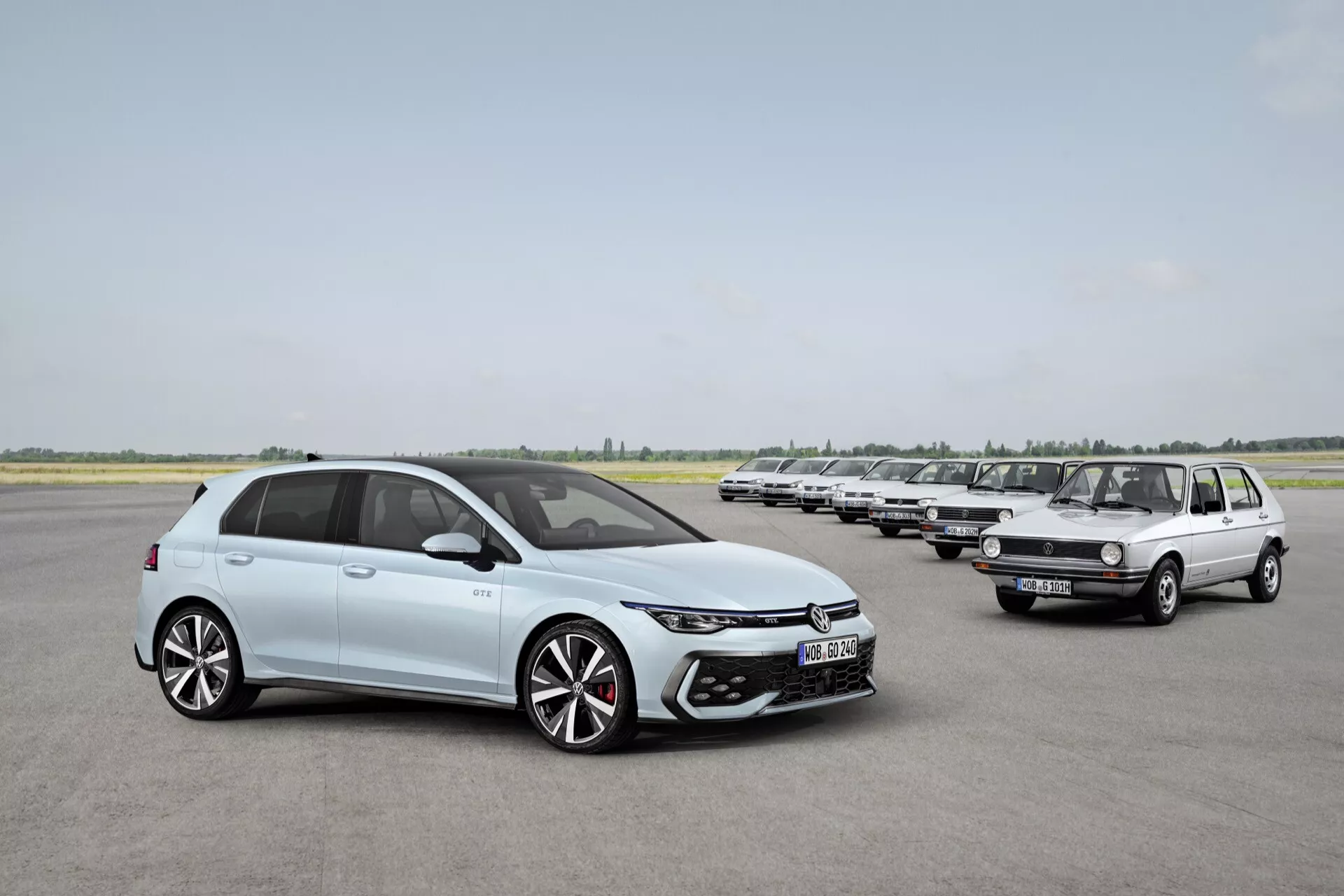 VW Golf 2024 (VIII-Facelift) v svetlomodrej farbe, moderný hatchback s LED svetlometmi, veľkým prívodom vzduchu, 18+ palcovými dvojfarebnými zliatinovými kolesami a elegantnými líniemi karosérie, prezentujúci evolúciu automobilového dizajnu vedľa staršej generácie modelu VW Golf na pristávacej dráhe.