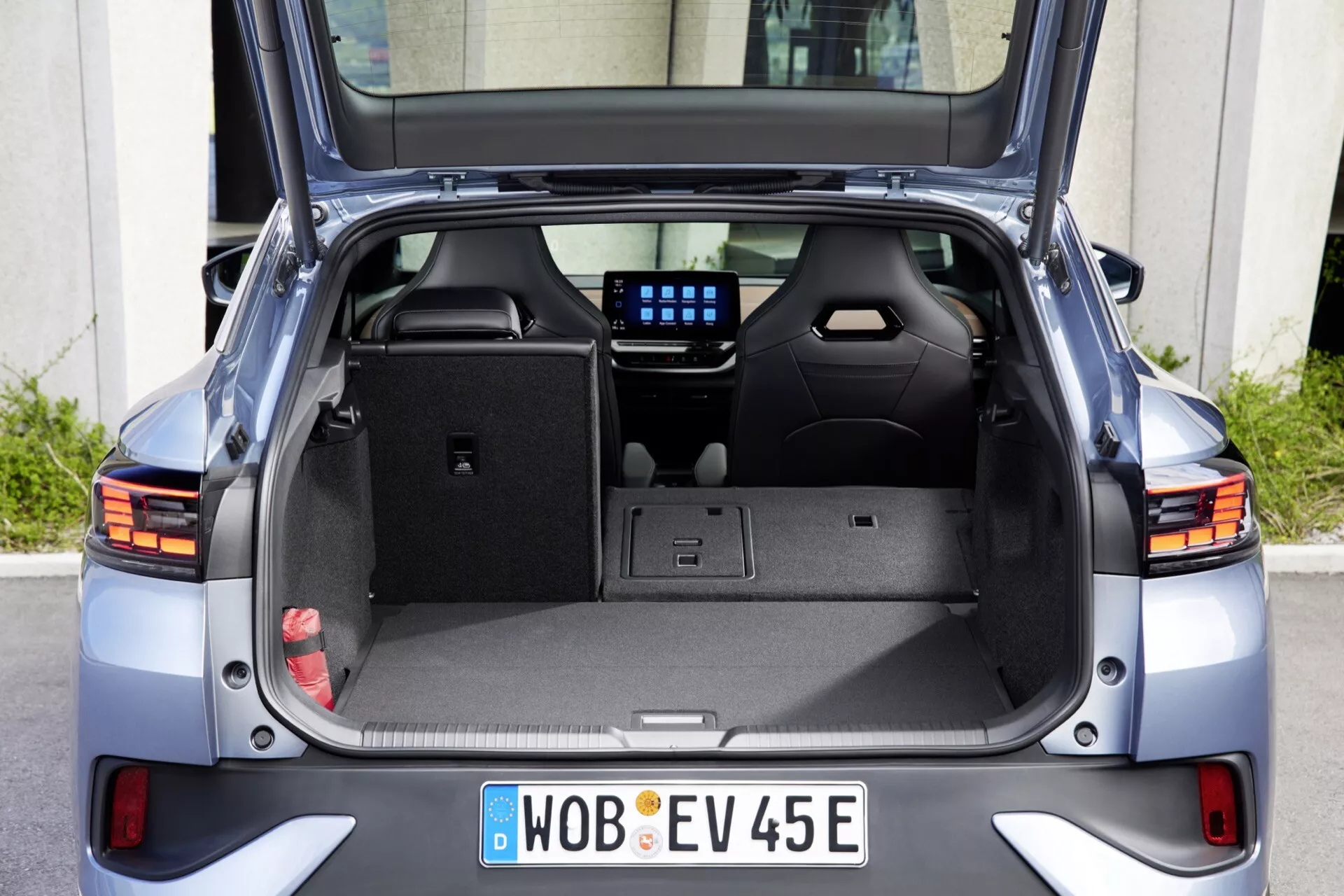 Pohľad zozadu na Volkswagen ID.5 2022 (1. generácia) zobrazujúci otvorený kufor, ktorý jasne ilustruje vnútorný priestor pre náklad, zadnú kabínu, zadné svetlá, zadný nárazník a stierač zadného okna. Fotografia zdôrazňuje prázdny priestor kufra s háčikmi, priehradkami, 12V zásuvkou a digitálnym displejom medzi zadnými sedadlami, ktorý ponúka pohľad na infotainment alebo klimatizačný systém vozidla.