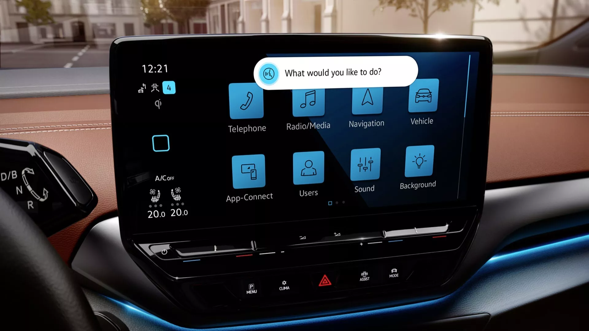 Tento obrázok zobrazuje interiér modelu 2022 VW ID.5 (1. generácia), konkrétne sa zameriava na centrálnu dotykovú obrazovku infotainmentu. Snímka je zhotovená z perspektívy sediaceho na prednom sedadle pasažiera alebo vodiča, zdôrazňujúc moderný displej s vysokým rozlíšením. Obrazovka je horizontálne orientovaná a obklopená minimálnym množstvom fyzických tlačidiel, s užívateľsky prívetivým rozhraním, ktoré obsahuje veľké ikony pre Telefón, Rádio/Media, Navigáciu, Nastavenia vozidla, App-Connect, Užívateľské profily, Nastavenia zvuku a Nastavenia pozadia. Displej tiež ukazuje automatickú dvojzónovú klimatizáciu nastavenú na 'lo' pre obe strany a hodiny ukazujúce čas 12:21. Pod obrazovkou sa nachádza niekoľko fyzických tlačidiel pre rýchly prístup k základným funkciám. Rozmazaný horný okraj prístrojovej dosky a modré ambientné osvetlenie v dolnej časti predného plánu zdôrazňujú prémiový interiér. Rozmazané pozadie cez čelné sklo naznačuje mestské prostredie.