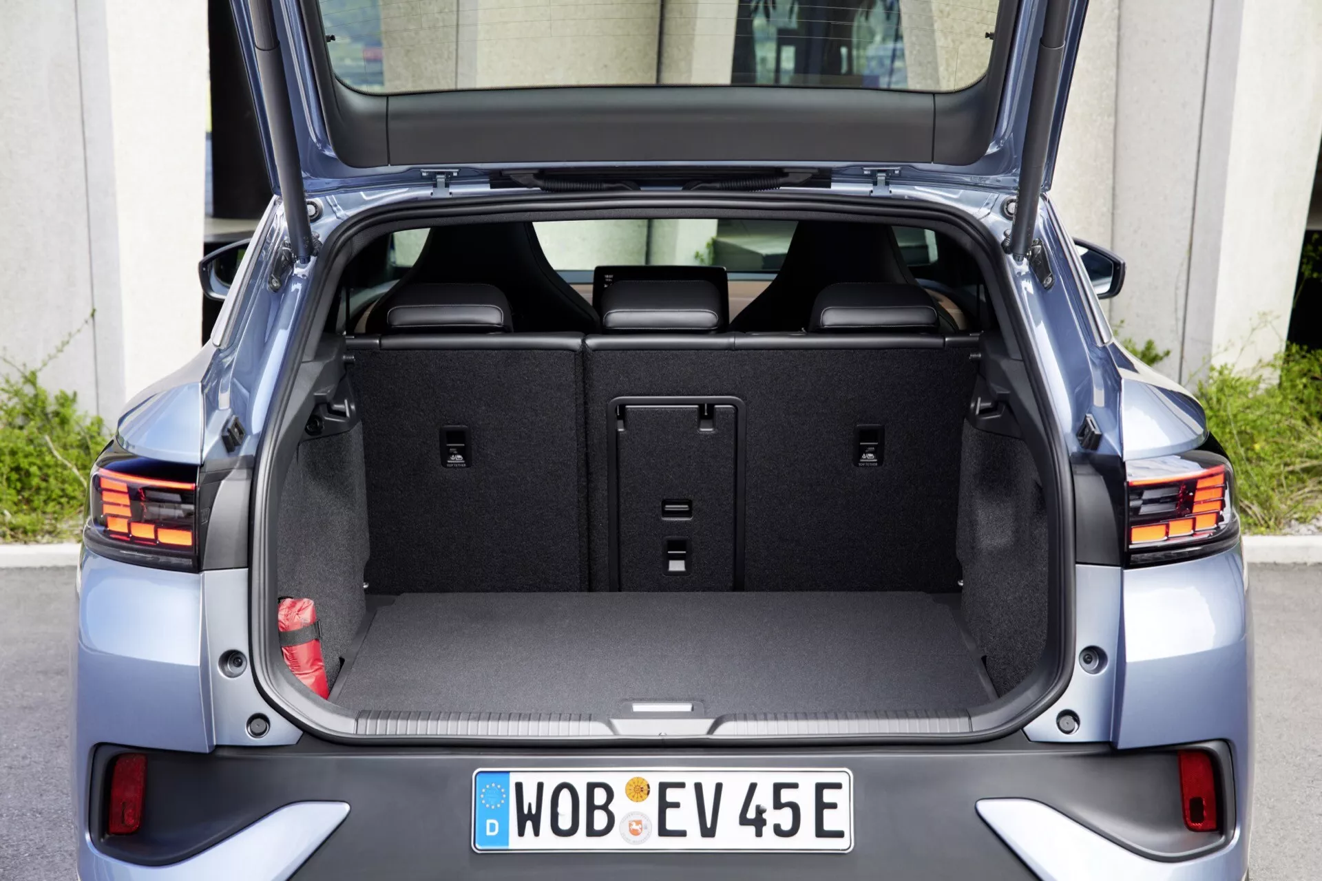 Zadný pohľad na moderný hatchback VW ID.5 2022 s otvoreným kufrom, ktorý ukazuje priestrannú prázdnu úložnú plochu, čistý kobercowy obklad, vzpriamené zadné sedadlá, integrované LED koncové svetlá, odrazky pri spodnom nárazníku, aerodynamický dizajn, parkovacie senzory na zadnom nárazníku, európsku EV poznávaciu značku a metalický povrch za denného svetla.
