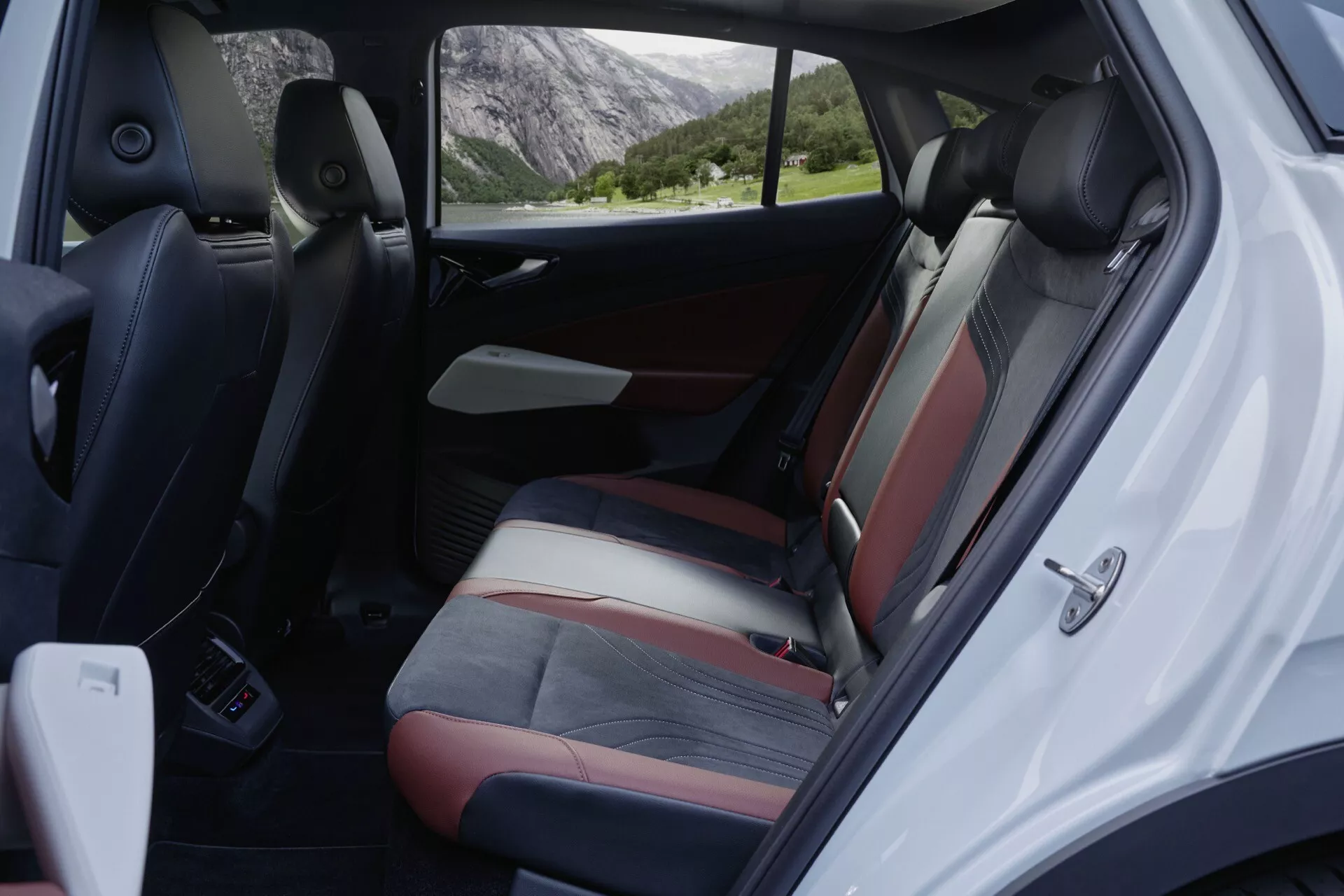 Pohľad do interiéru VW ID.5 2022 (1. generácia) ukazujúci dvojfarebné zadné sedadlá a dverový panel, vyfotografovaný z ľavej strany auta s otvorenými zadnými dverami. Tmavé stredné časti sedadiel naznačujú materiál ako koža alebo koženka so svetlejším bočným čalúnením. Viditeľné sú opierky hlavy, bezpečnostné pásy, ovládanie elektrických okien, mriežka reproduktora a kotvové body pre detské bezpečnostné sedadlo. Dverový panel zodpovedá farebnej schéme sedadiel a zahŕňa úložné vrecko. Auto je zaparkované v prírodnom, možno vidieckom prostredí.