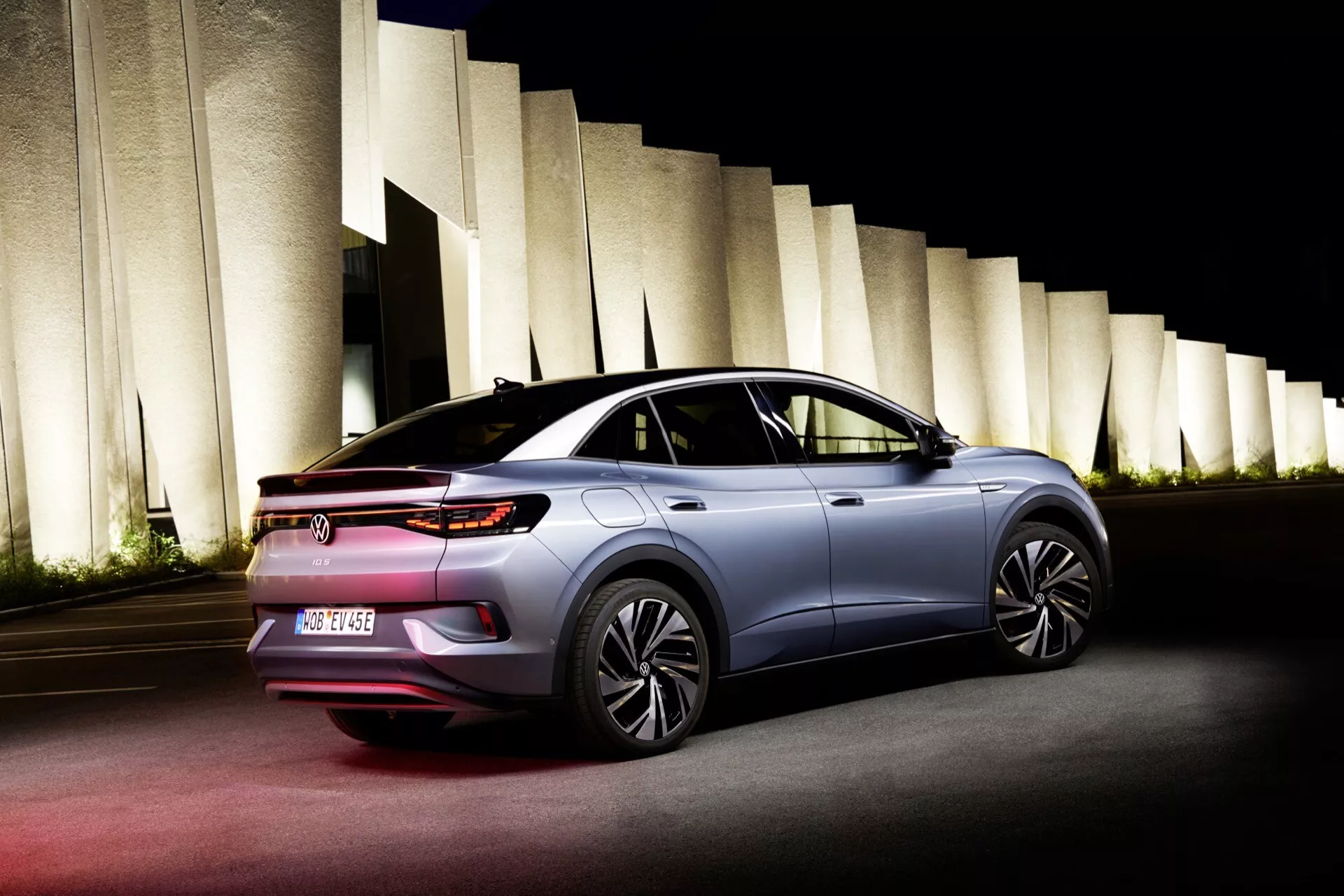 Zadný trojštvrťový pohľad na VW ID.5 2022 (1. generácia), zobrazujúci štíhly tvar, strechu ako kupé, zadné svetlá LED, aerodynamické bočné zrkadlá a moderné kolesá, zachytené v noci s umelým osvetlením, ktoré zvýrazňuje vozidlo a architektonické prvky v pozadí.