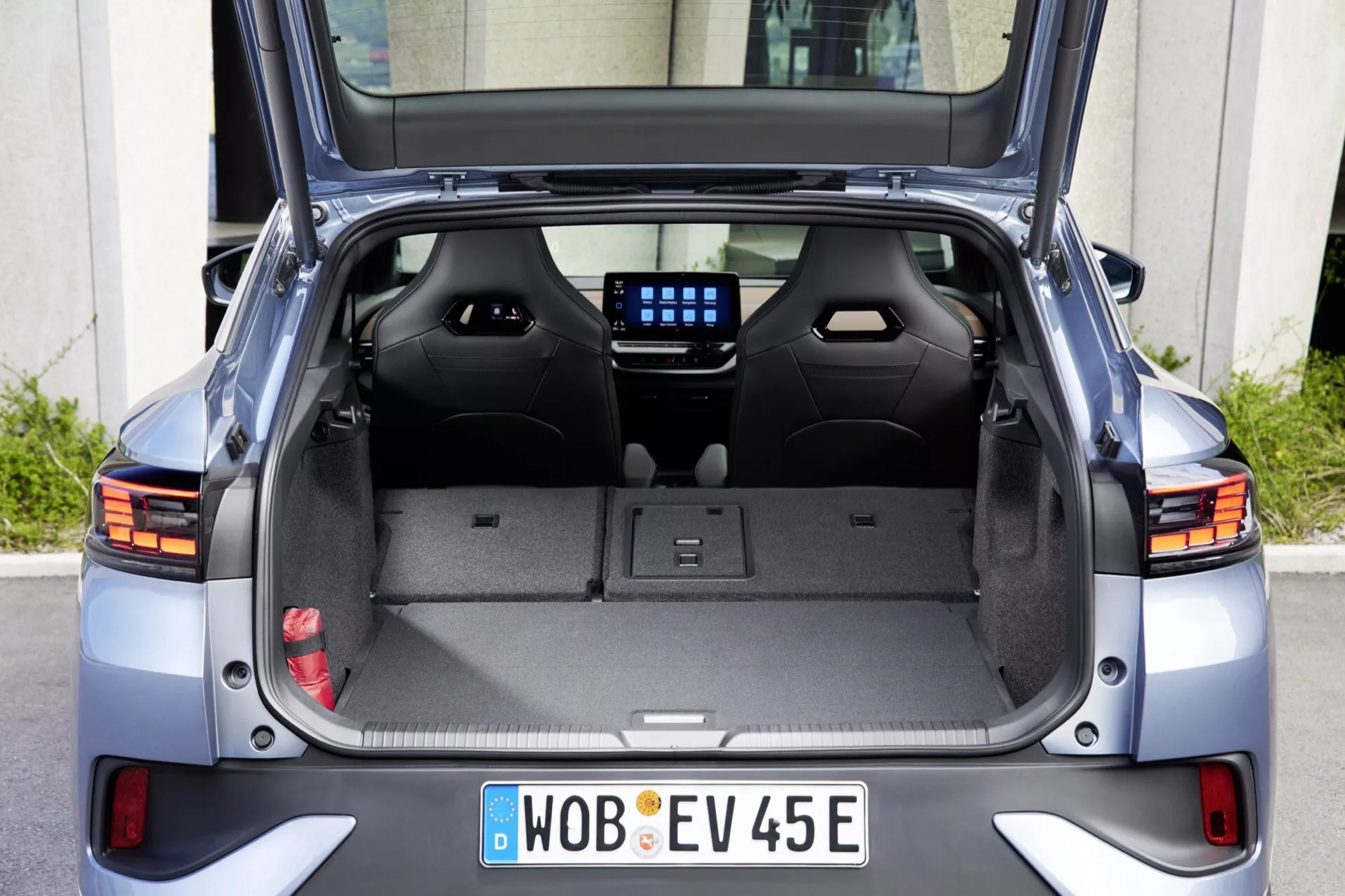 Zadný pohľad na Volkswagen ID.5 2022 (prvá generácia) s otvoreným kufrom, ukazujúc priestrannú kapacitu prepravy so sklopenými zadnými sedadlami, čalúneným interiérom, zasunutým zatahovacím krytom nákladu, plastovo obloženými dverami kufra, ohrevnými prvkami na zadnom skle, zadným stieračom, čiastočne viditeľnými modernými LED zadnými svetlami a nemeckou registračnou značkou EV z Wolfsburgu, naznačujúcou dizajn elektrického vozidla a všestranné usporiadanie prepravy.