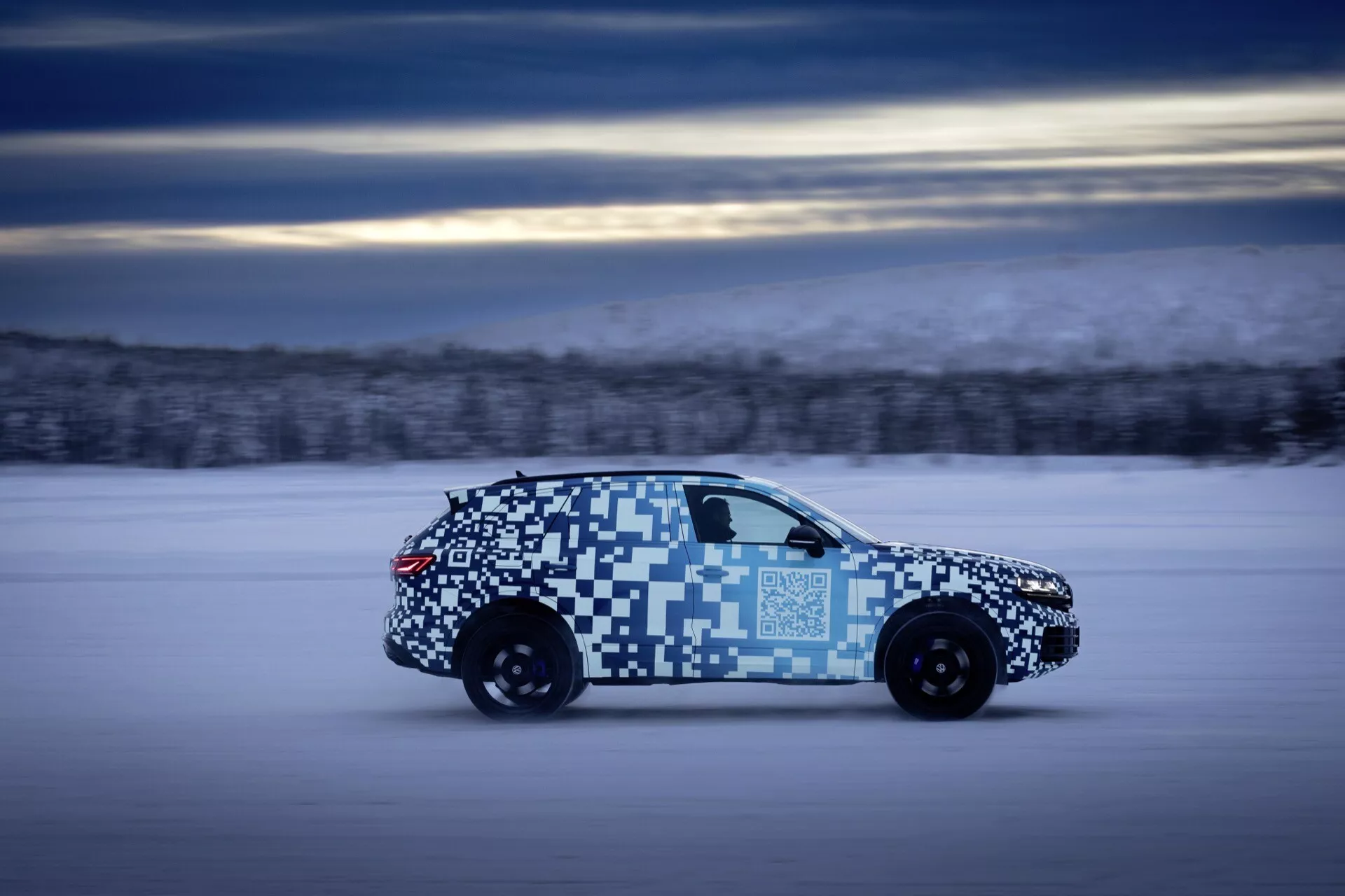 VW Touareg 2023 (III-Facelift) v pohybe, zdôrazňujúc jeho aerodynamický dizajn a LED zadné svetlá, s maskovacím obalom, v zimnom testovacom prostredí