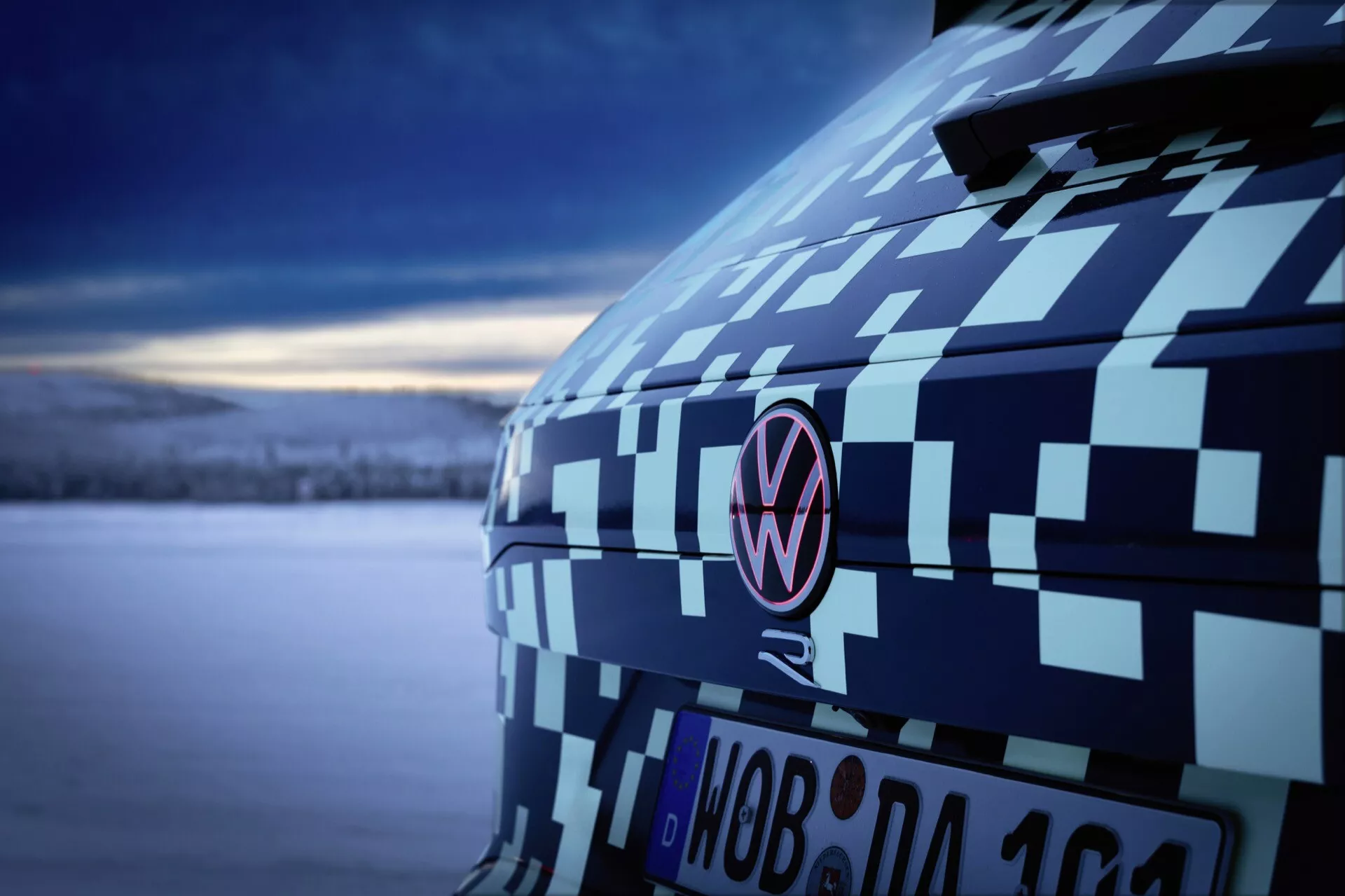 Zblízka pohľad na zadnú časť Volkswagena Touareg (III Facelift) rok 2023 s maskovacou fóliou zvýrazňujúcou C-stĺpik a emblem pri súmraku, prezentujúci testovanie prototypov automobilov a dizajn za mäkkého, chladného osvetlenia