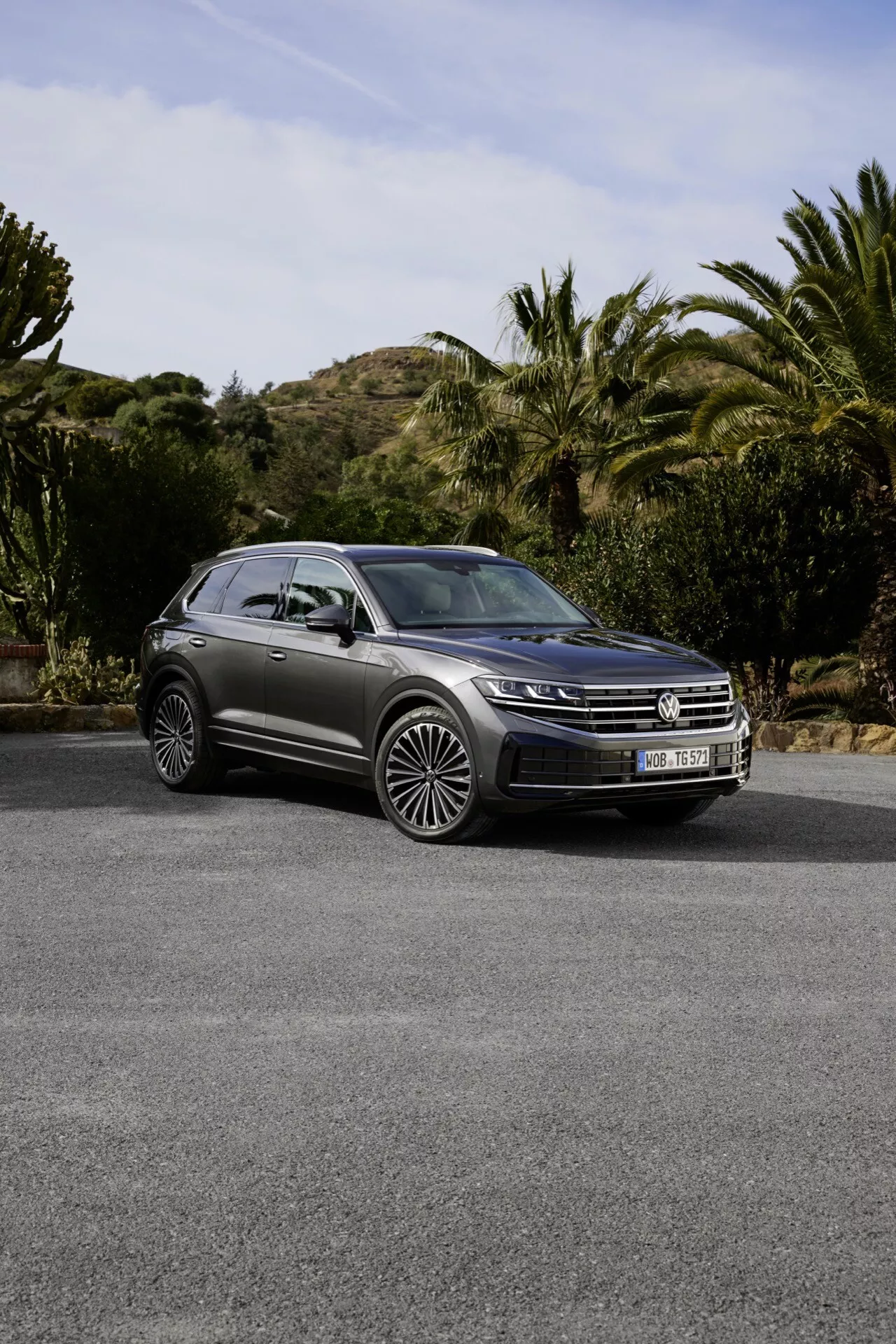 Model VW Touareg III facelift 2023 zaparkovaný vonku s prednou mriežkou, LED svetlometmi, panoramatickou strechou a viacramennými zliatinovými kolesami proti scénickému pozadí jemných kopcov, kríkov a stromov, čo zvýrazňuje jeho luxusný SUV dizajn a pokročilé funkcie.