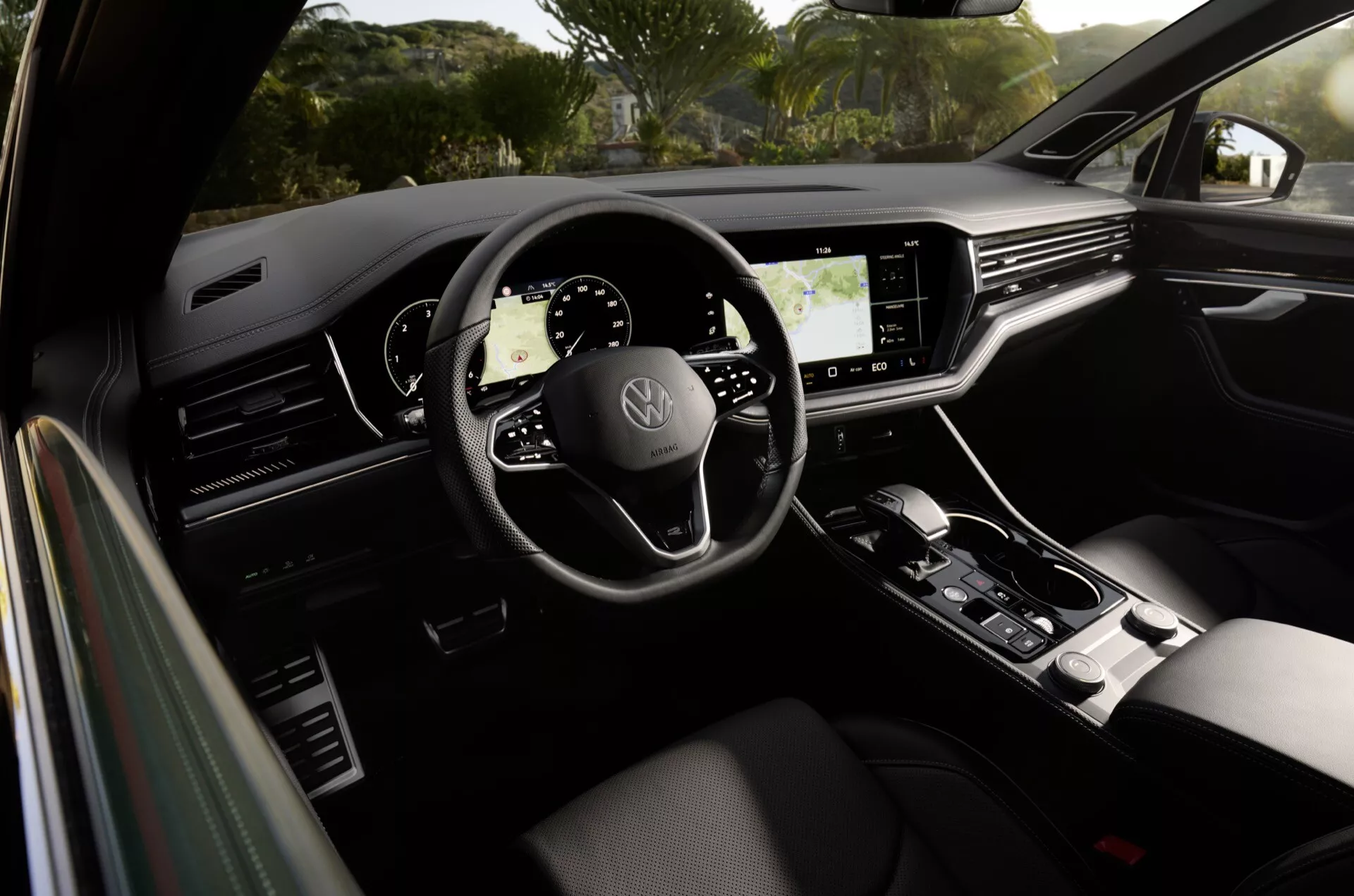 Interiér Volkswagen Touareg 2023 ukazujúci volant s tromi ramenami s logom značky, plne digitálny prístrojový panel, veľký dotykový infotainment displej a štýlovú radicu páku, zdôrazňuje moderný dizajn auta a pokročilé technologické funkcie