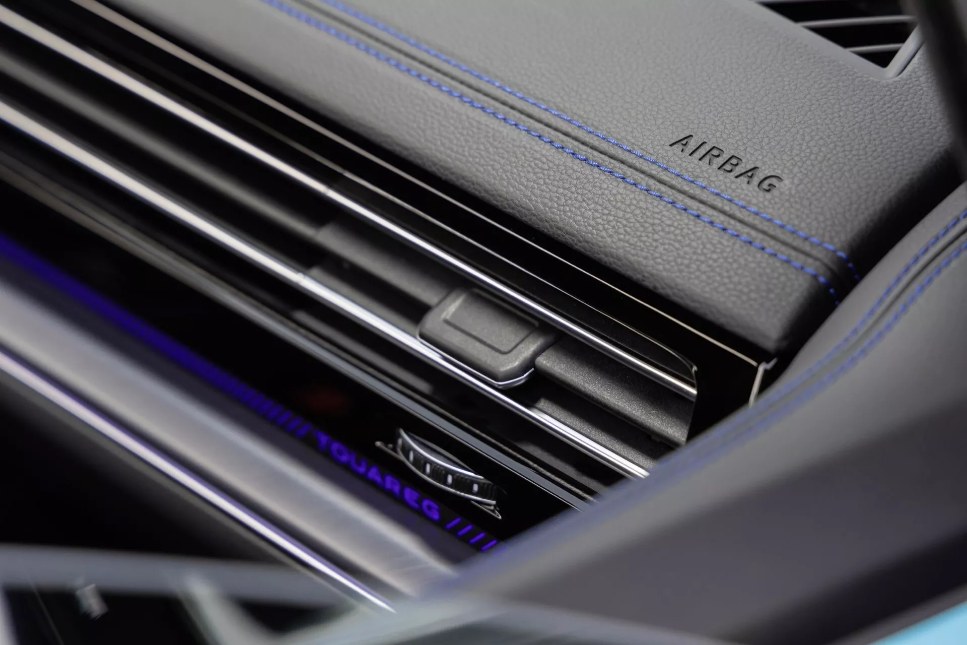 Detailný pohľad na interiér VW Touareg 2023 (III-facelift) ukazujúci detail vetracej mriežky na prístrojovej doske s ovládaním klimatizácie pre dve zóny, kontrastné modré šitie a ambientné osvetlenie