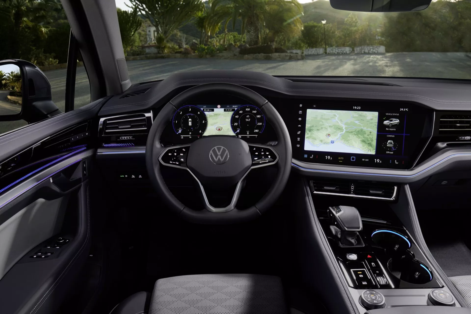 Interiér Volkswagen Touareg III facelift 2023 z pohľadu zadných sedadiel smerom k digitálnemu prístrojovému panelu v dennom svetle, predstavuje multifunkčný volant s logom, digitálny prístrojový panel, veľký dotykový systém infotainment s GPS, elegantné dotykové ovládanie klímy, minimalistickú páčku automatickej prevodovky a centrálny panel s ambientným osvetlením, vysokej kvality a bezpečnostnými prvkami