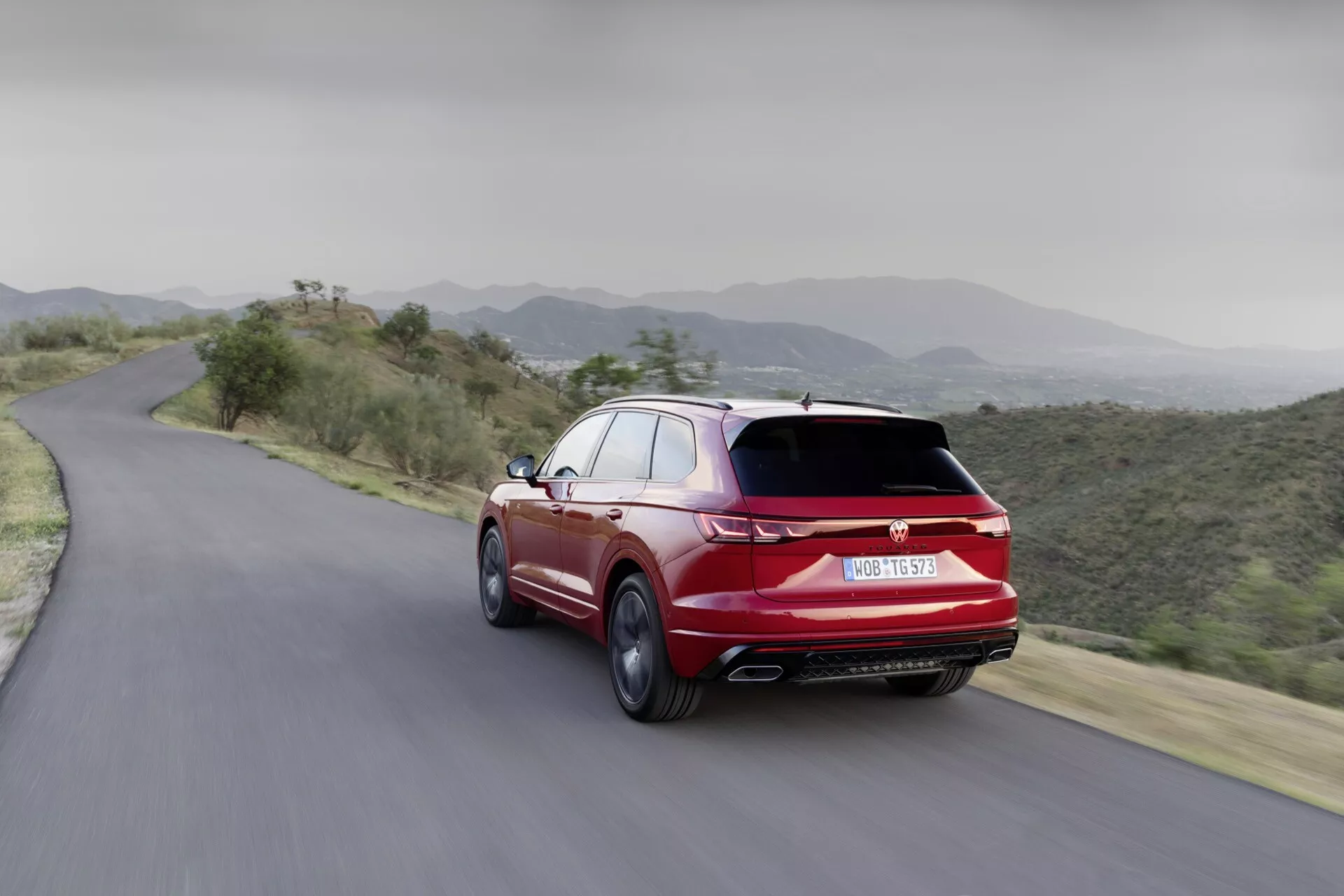Dynamický zadný pohľad na VW Touareg 2023 na horskej ceste, predvádzajúci aerodynamický dizajn, dvojité výfuky a športovú úpravu vo výraznej červenej