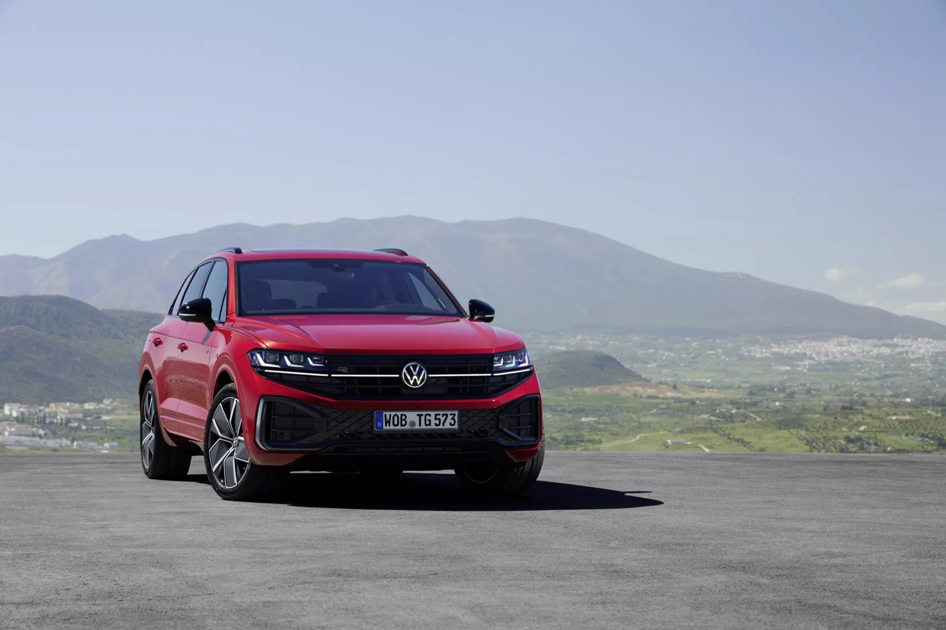 Volkswagen Touareg 2023 (III-Facelift) predstavuje svoj moderný dizajn z nízkeho uhla z prednej trojštvrtinovej strany zdôrazňujúci LED svetlomety, športový predný nárazník, aerodynamickú mriežku a viaceré hovoriace zliatinové kolesá na pozadí malebnej krajiny.