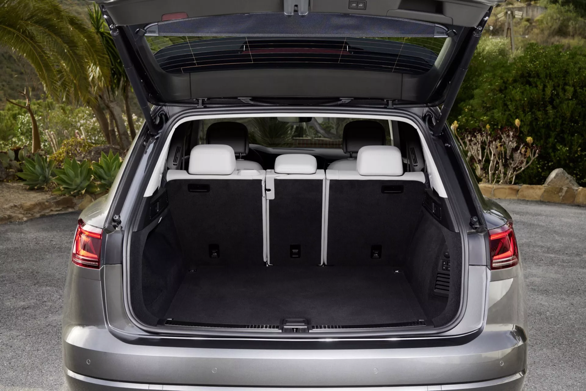 VW Touareg III-facelift 2023 zobrazený zo zadného uhla s otvoreným kufrom predvádzajúcim priestranný nákladný priestor, plochú nákladnú plochu a stiahnutý kryt nákladu, čím zdôrazňuje moderný dizajn a pokročilé bezpečnostné funkcie SUV