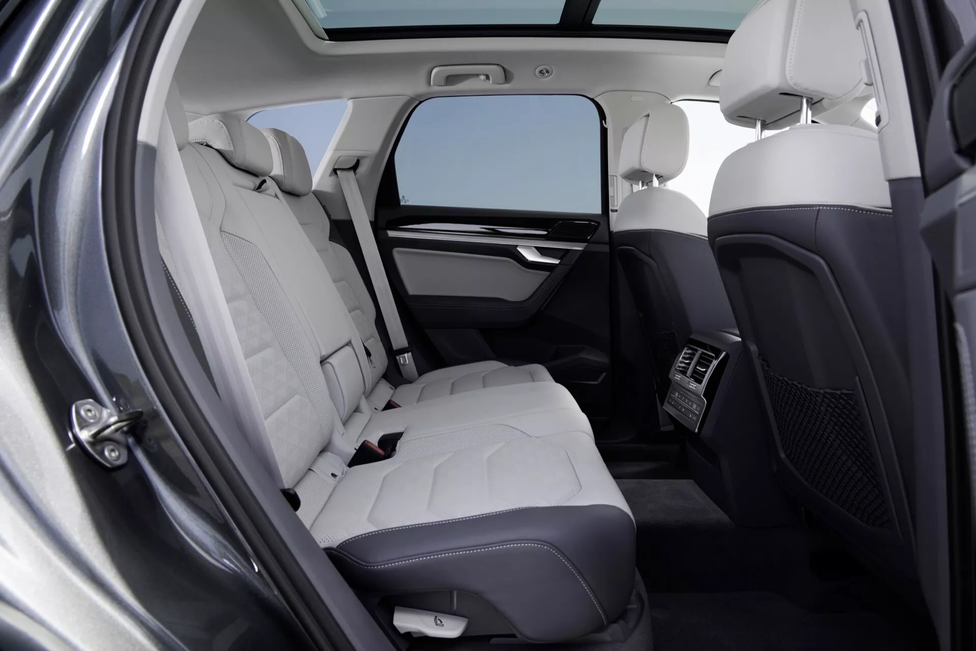 Pohľad do interiéru VW Touareg 2023 (III-Facelift) sústreďujúci sa na luxusnú oblasť zadných sedadiel s koženými sedadlami svetlej farby, klimatizáciou a prémiovými detailmi kabíny z perspektívy otvorených zadných ľavých dverí.