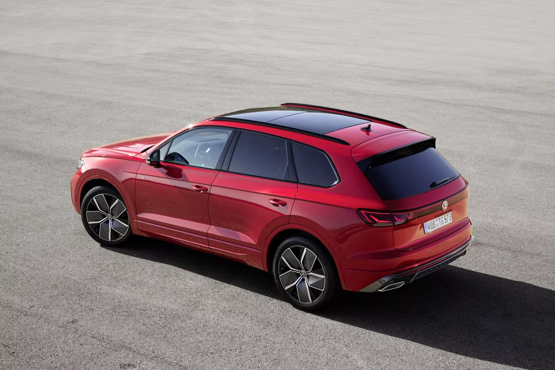 VW Touareg III po facelifte z roku 2023 z vysokého zadného trojštvrťového uhla ukazuje jeho elegantnú siluetu, charakteristické línie, líniu strechy, detailný dizajn zadného spoilera a antén, inovatívny tvar a dizajn zadných svetiel a nárazníka, jasne viditeľné kolesá so štýlovými diskami, zadné čelné sklo, prvky dizajnu zadných dverí s kľučkami a lemovaním, s náznakmi predných dverí a bočných spätných zrkadiel, predvádzajúce technologické funkcie ako sú zadné parkovacie senzory, vysoko umiestnené brzdové svetlo, LED alebo OLED technológia zadných svetiel a možno aerodynamické pridatky na zadnom nárazníku, zvýrazňujúce proporcie a postoj vozidla.